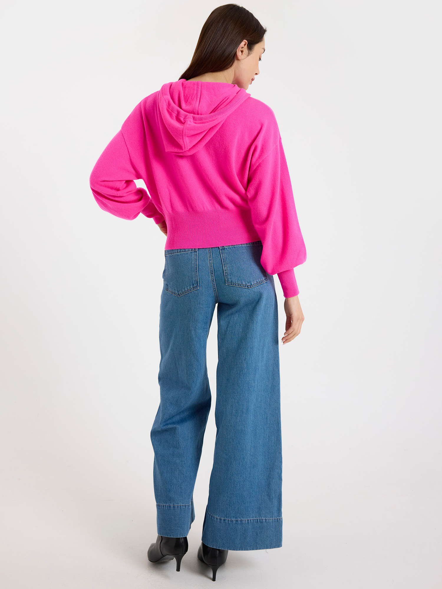 Woman wearing a bright pink hoodie and blue jeans on a white background
