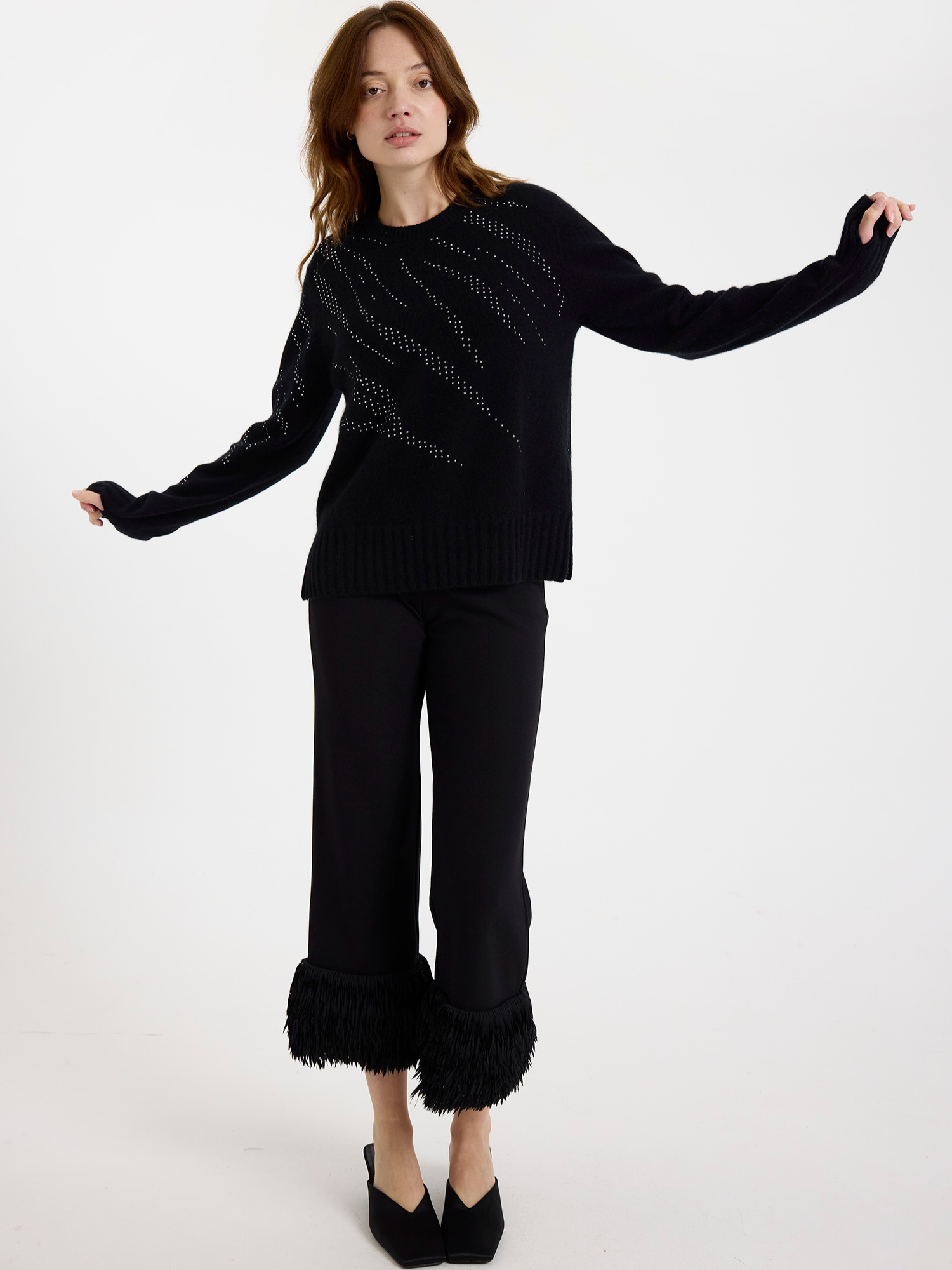 Woman wearing a black sweater with silver stud zebra pattern and black pants with ruffled cuffs on a white background