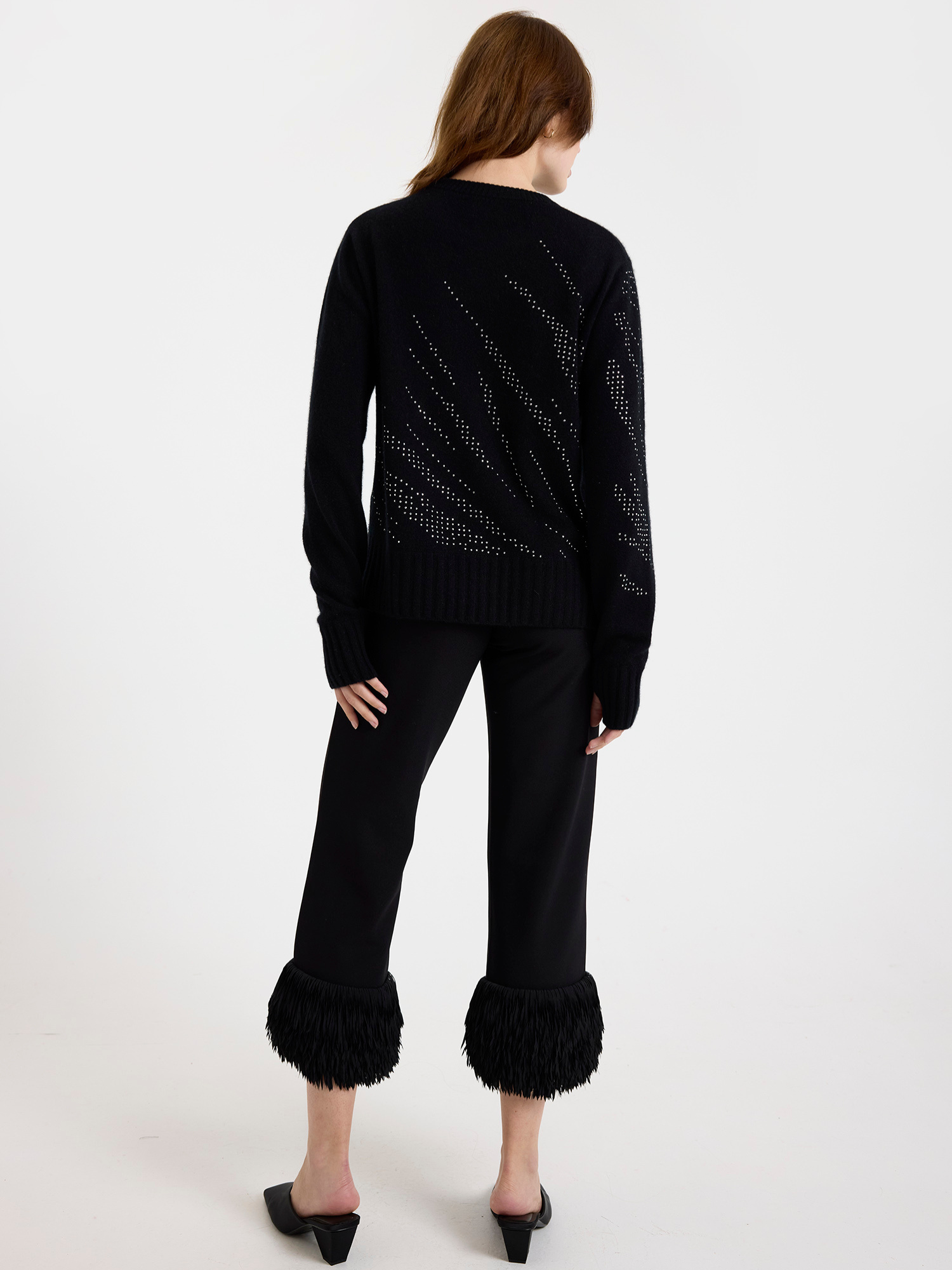 Woman wearing a black sweater with silver stud zebra pattern and black pants with ruffled cuffs on a white background