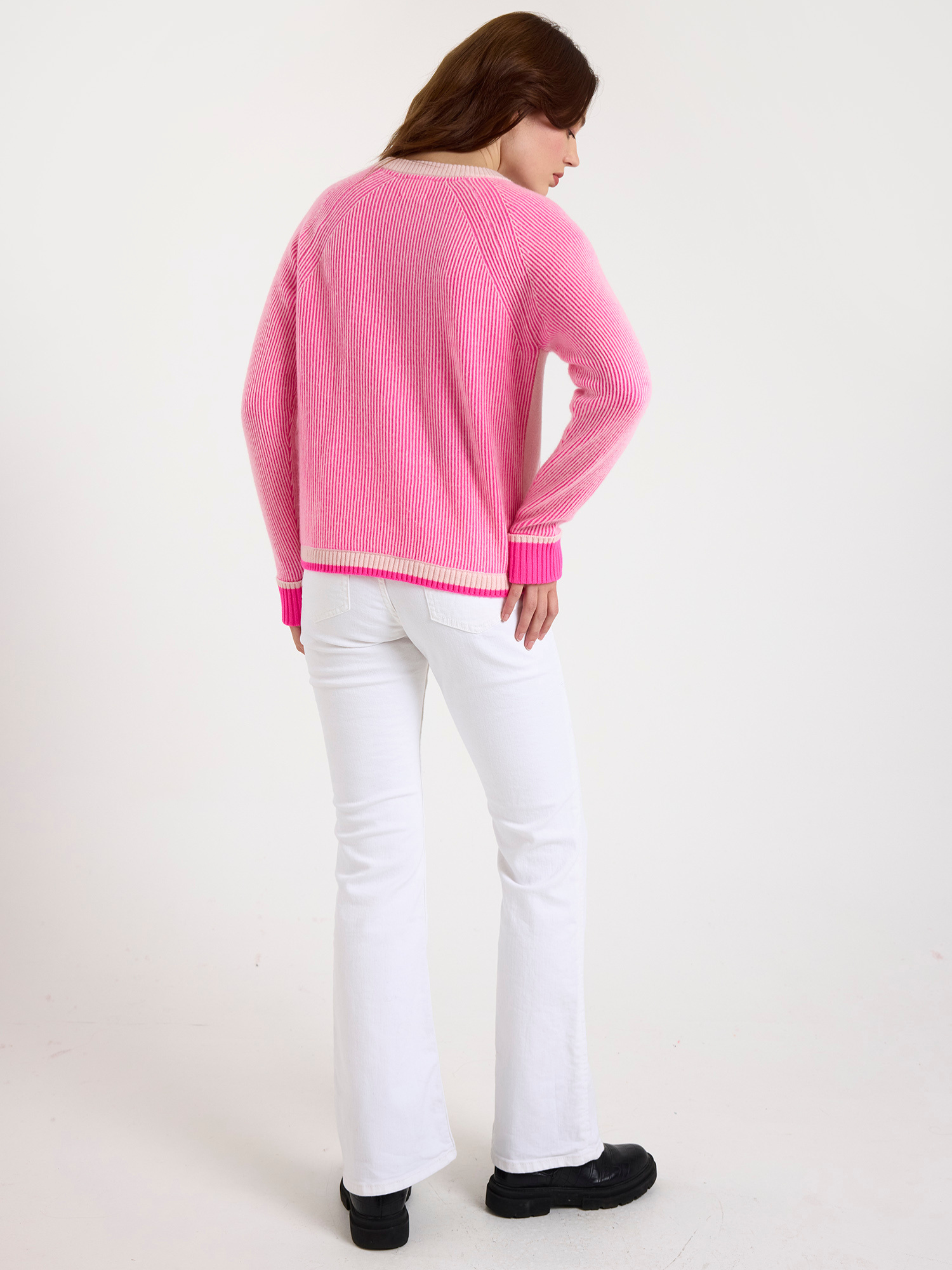 woman wearing a ribbed pink sweater and white jeans on a white background