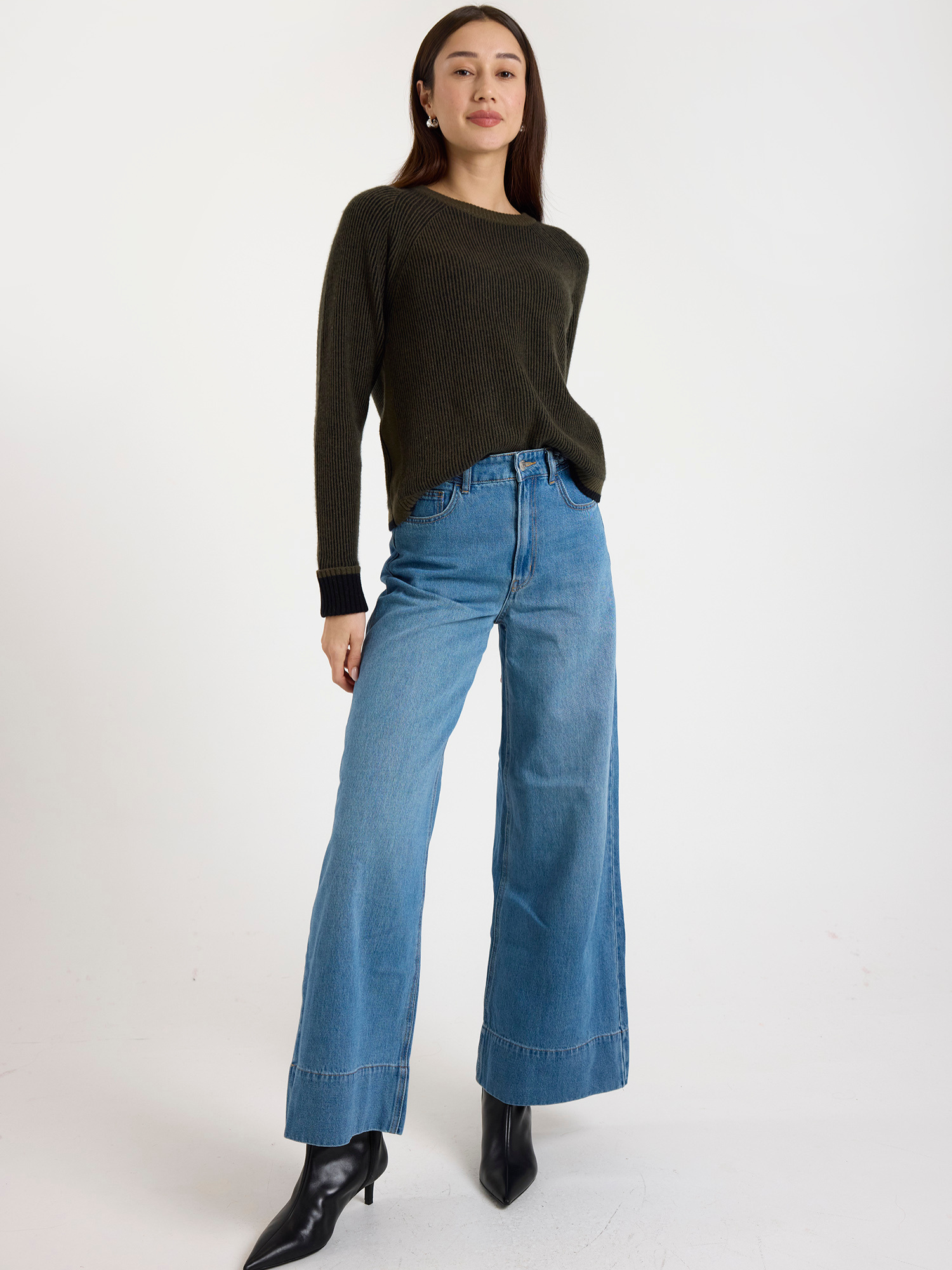 Woman wearing a ribbed dark green sweater and blue jeans on a white background