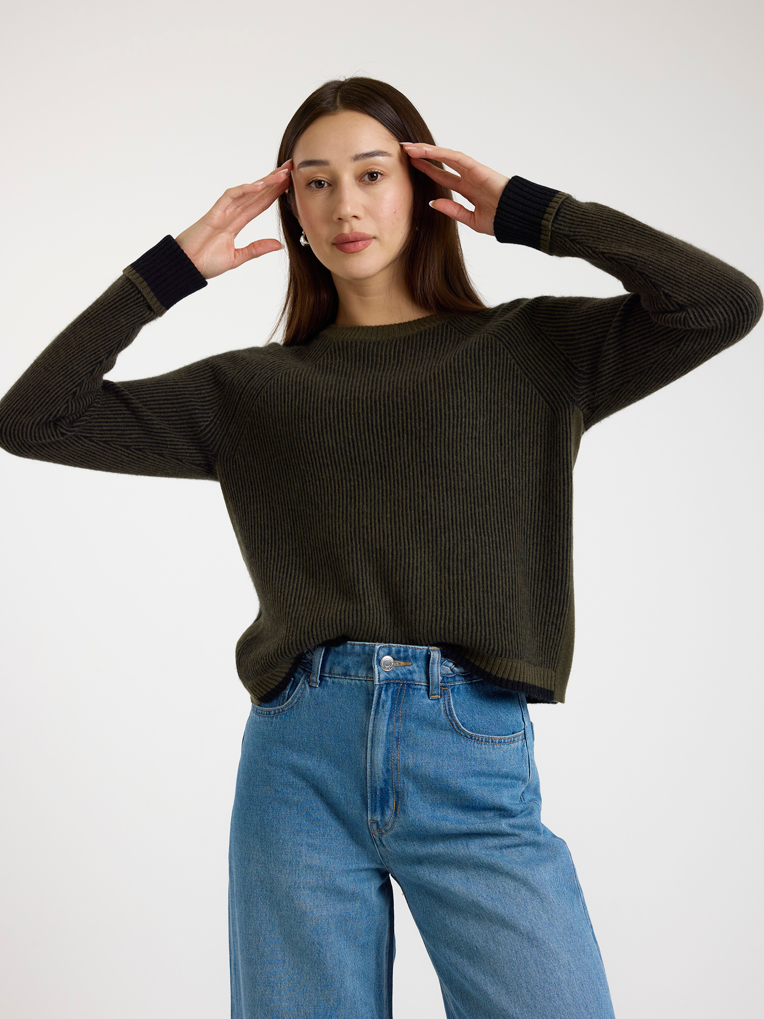 Woman wearing a dark green ribbed sweater and blue jeans on a white background