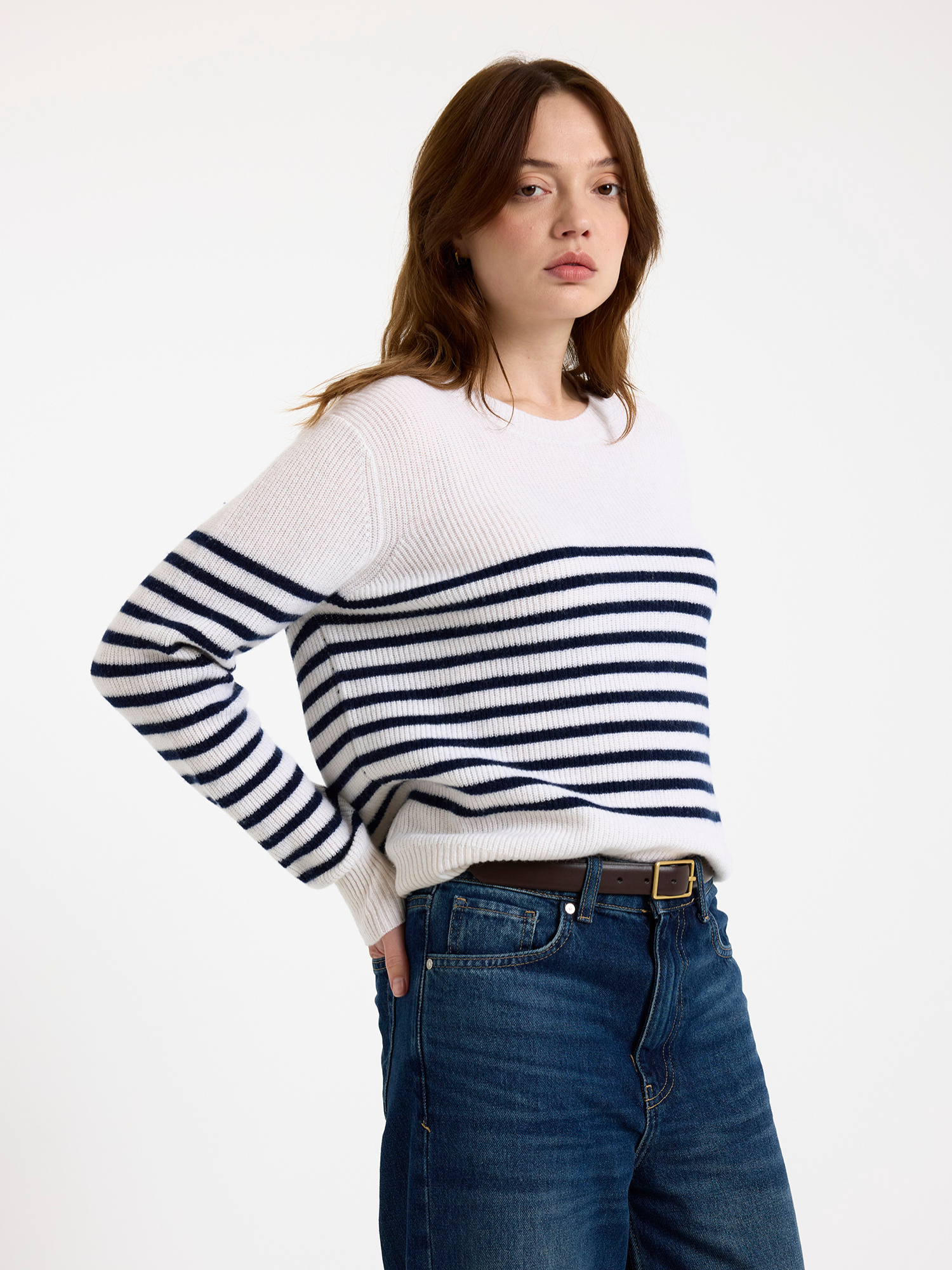 Woman wearing a white sweater with blue stripes and blue jeans on a white background