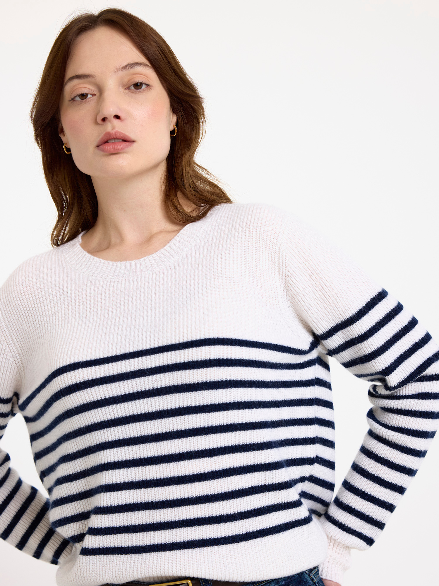 Woman wearing a white sweater with blue horizontal stripes on a plain background