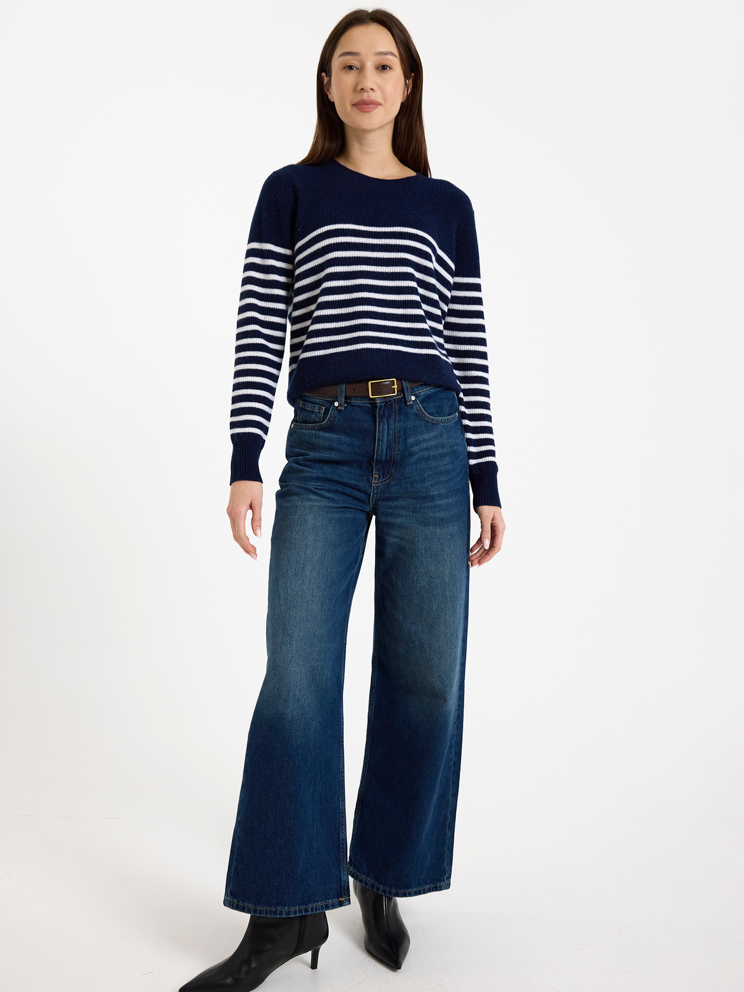 Woman wearing a navy and white striped sweater with high-waisted blue jeans on a white background