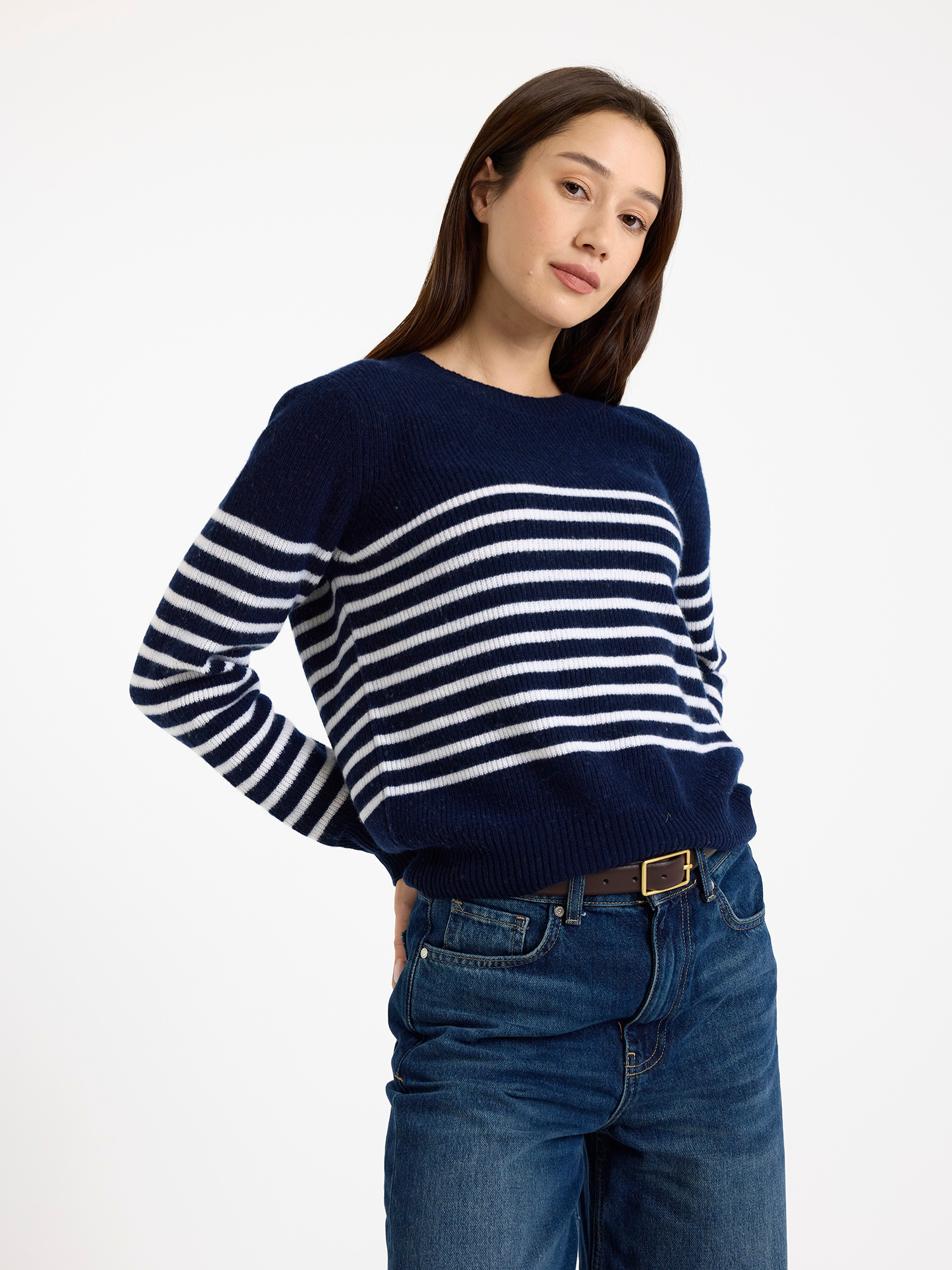 Woman wearing a navy and white striped sweater with blue jeans on a white background