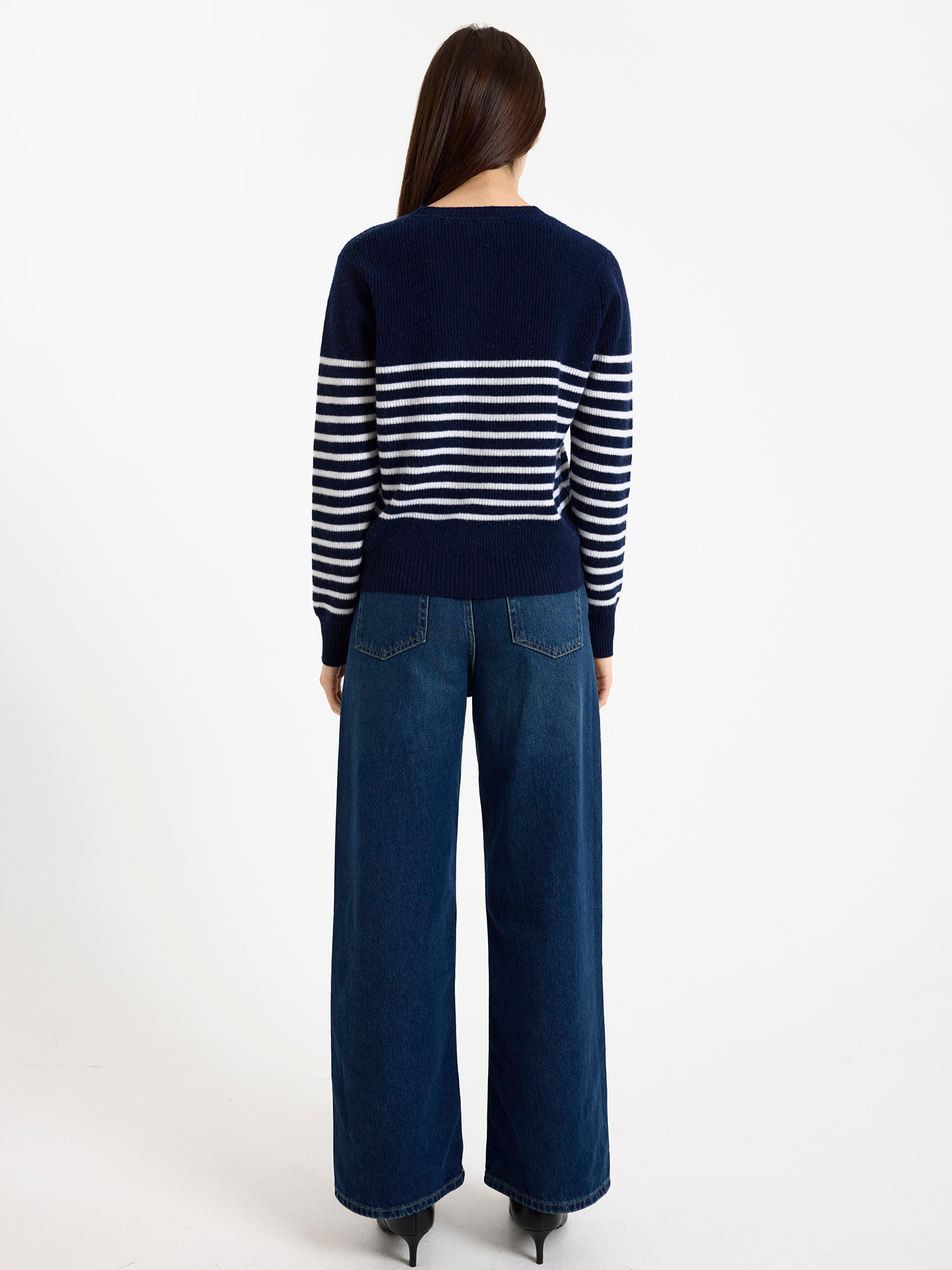 Woman wearing a navy and white striped sweater with blue jeans on a white background
