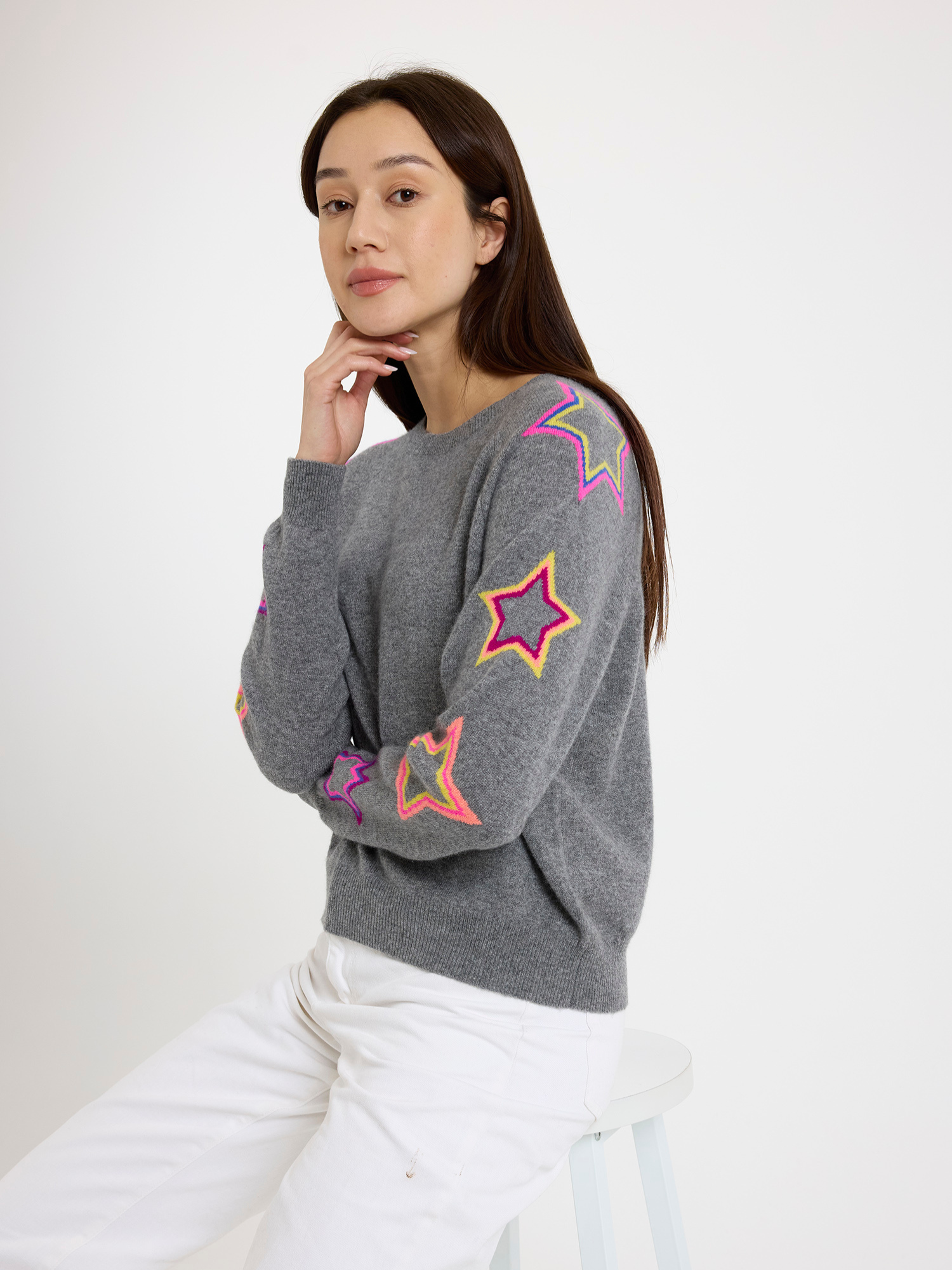 Woman wearing a grey sweater with colourful star patterns on a white background