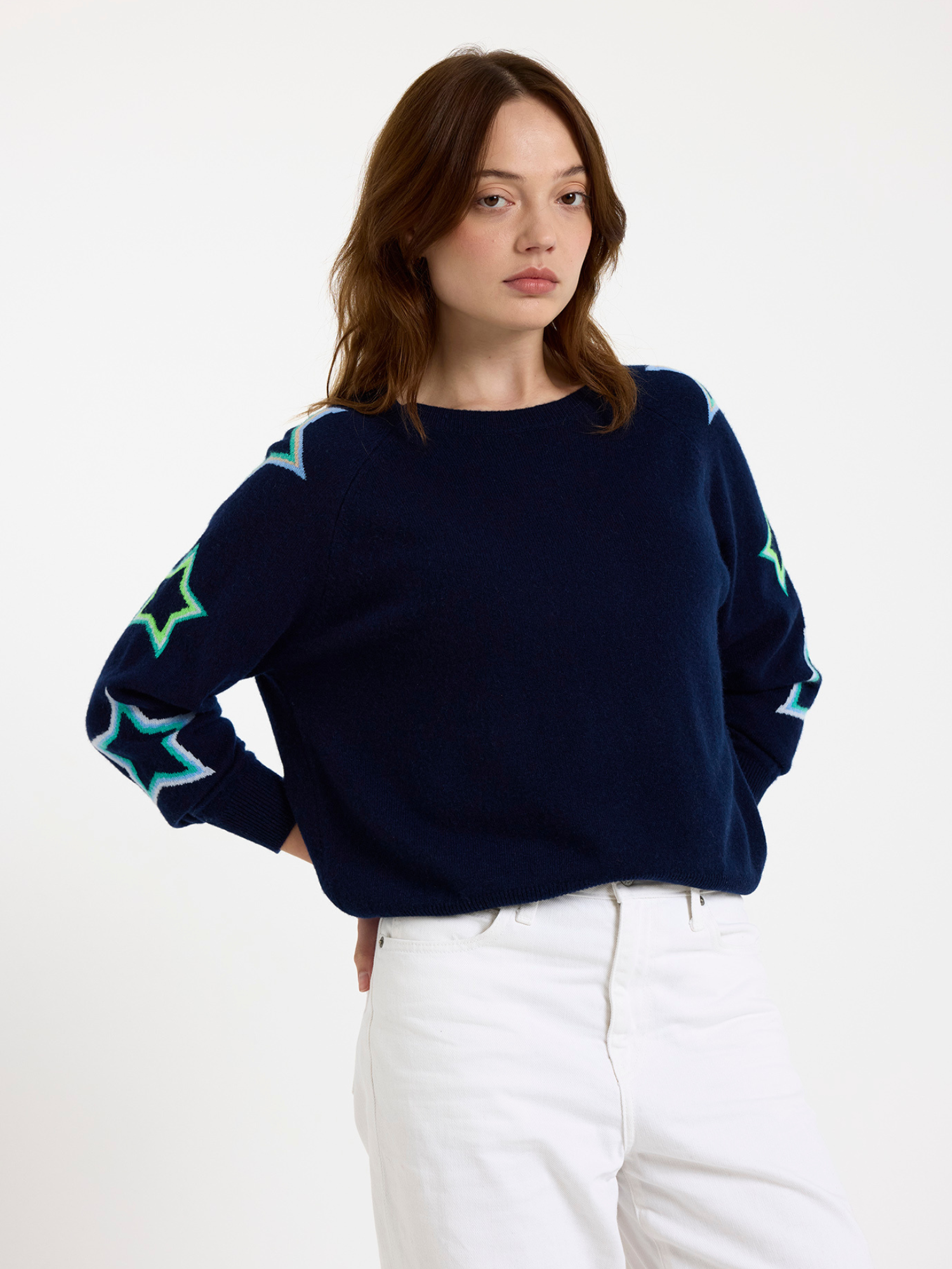 Woman wearing a navy sweater with star patterns on the sleeves against a white background