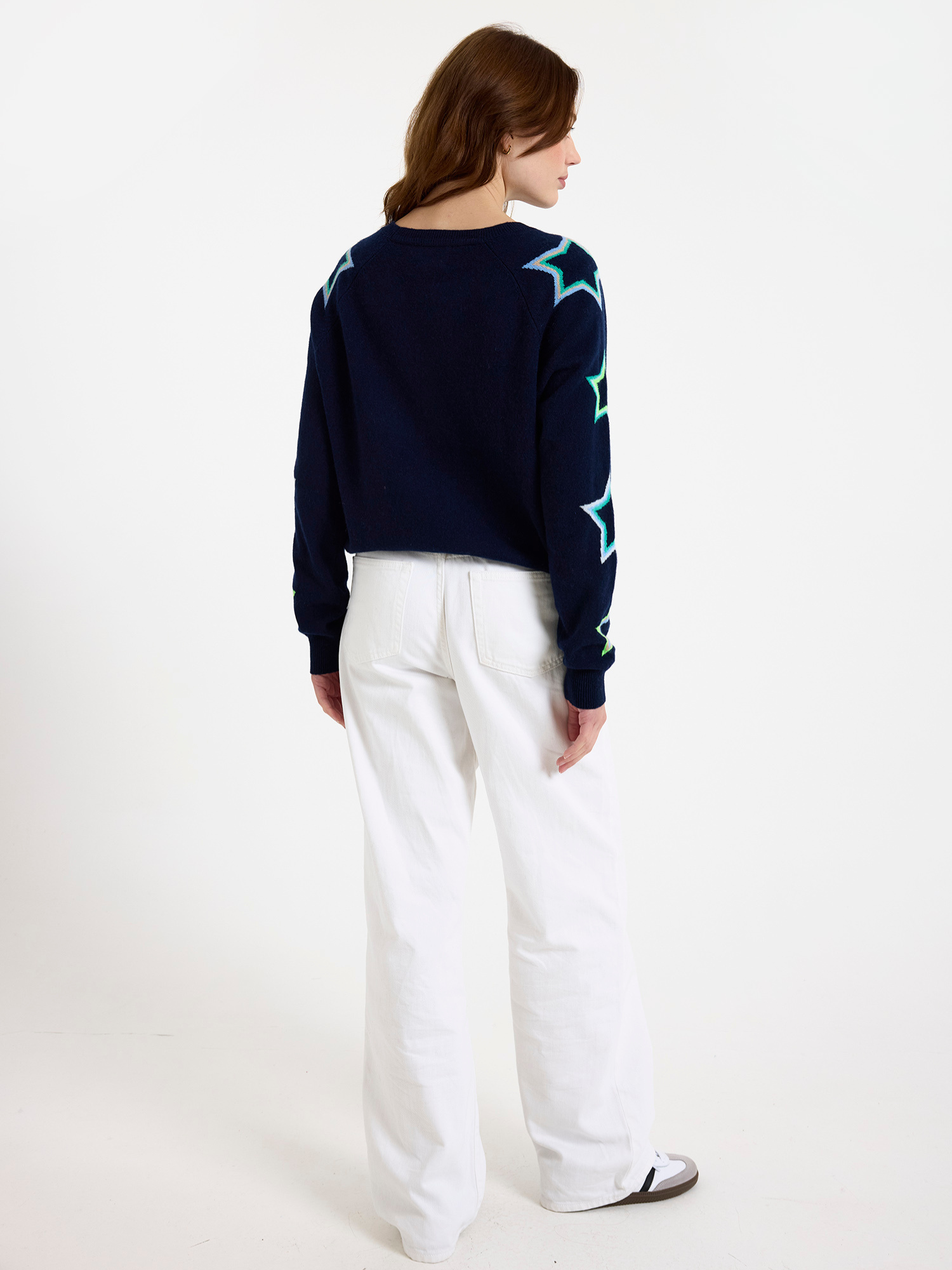 Woman wearing a navy sweater with star patterns and white jeans on a white background