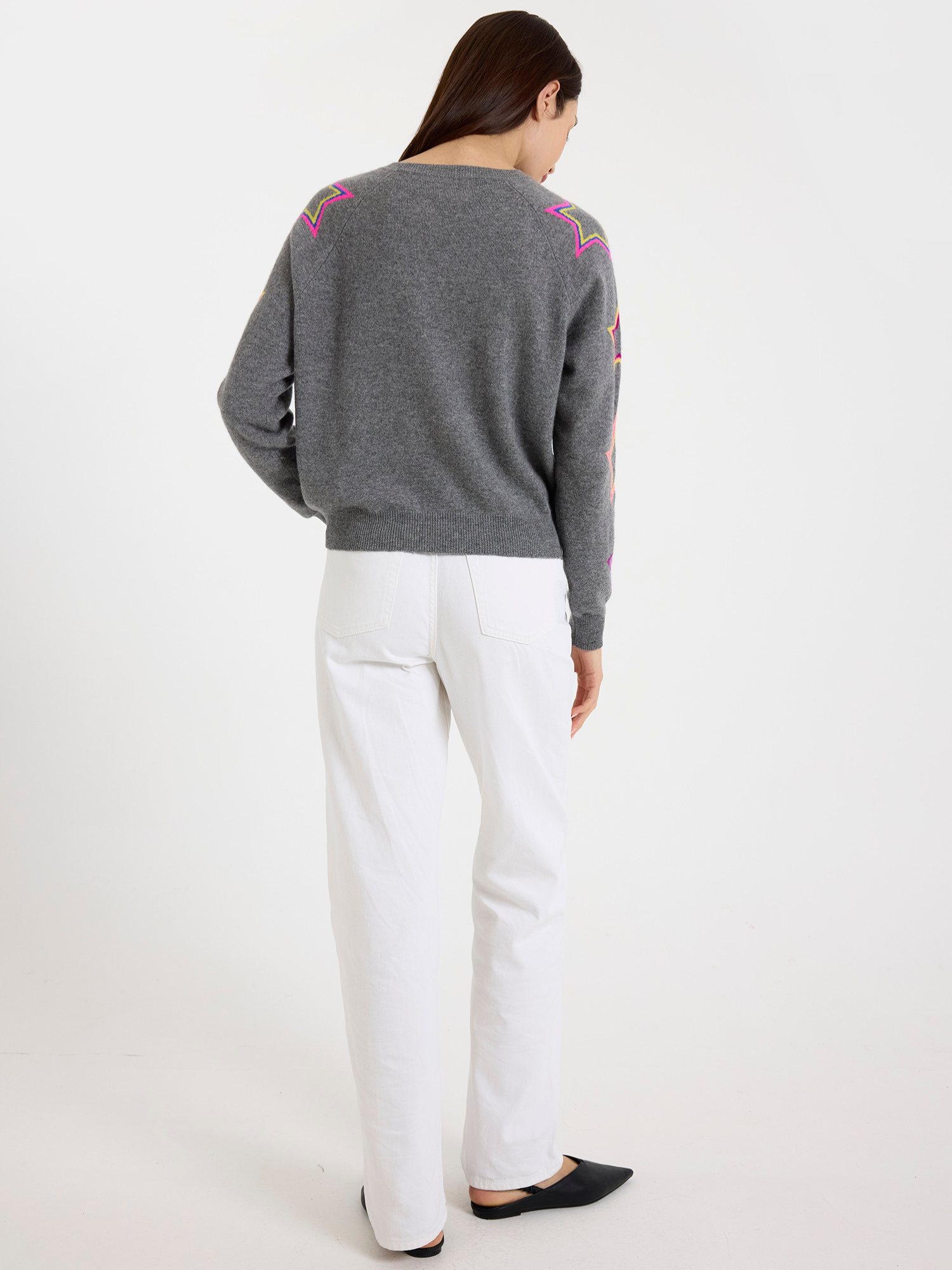 Woman wearing a grey sweater with colourful star patterns on a white background