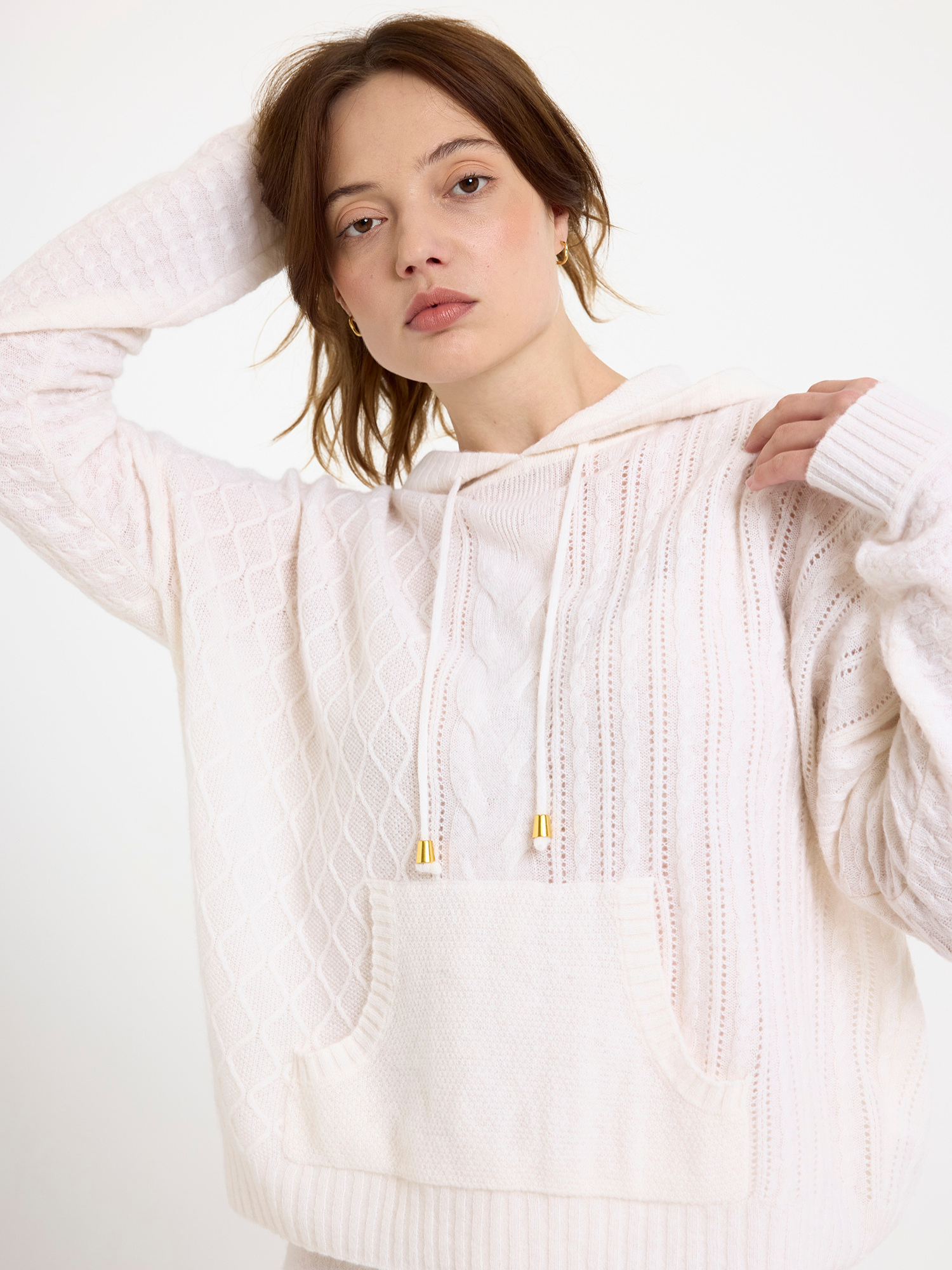 Woman wearing a white cable knit hoodie on a plain background