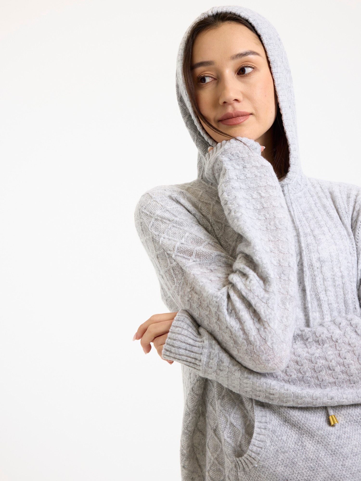 Woman wearing a grey cable knit hooded sweater on a white background