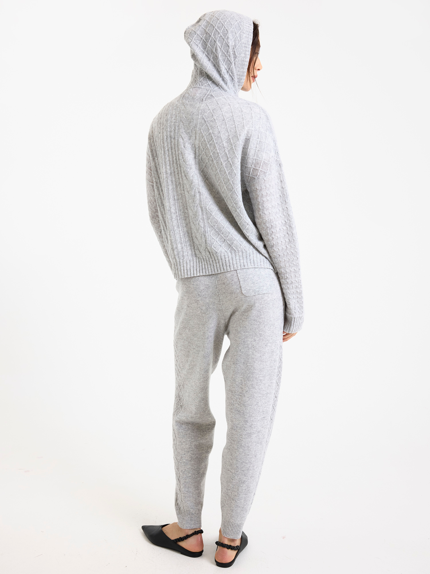 Woman wearing a grey cable knit hoodie and joggers on a white background