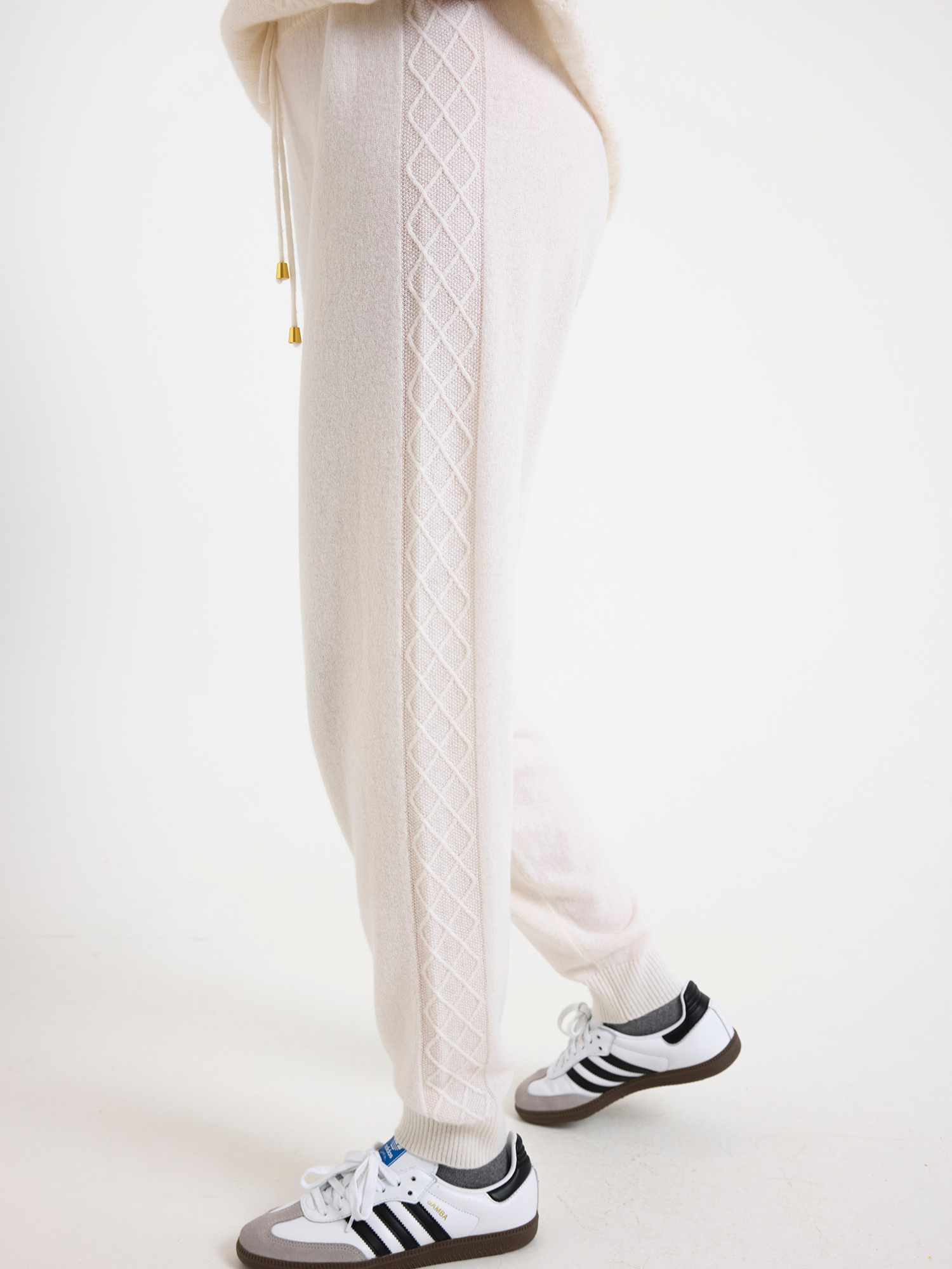 White cable-knit joggers with black Adidas sneakers on a white background