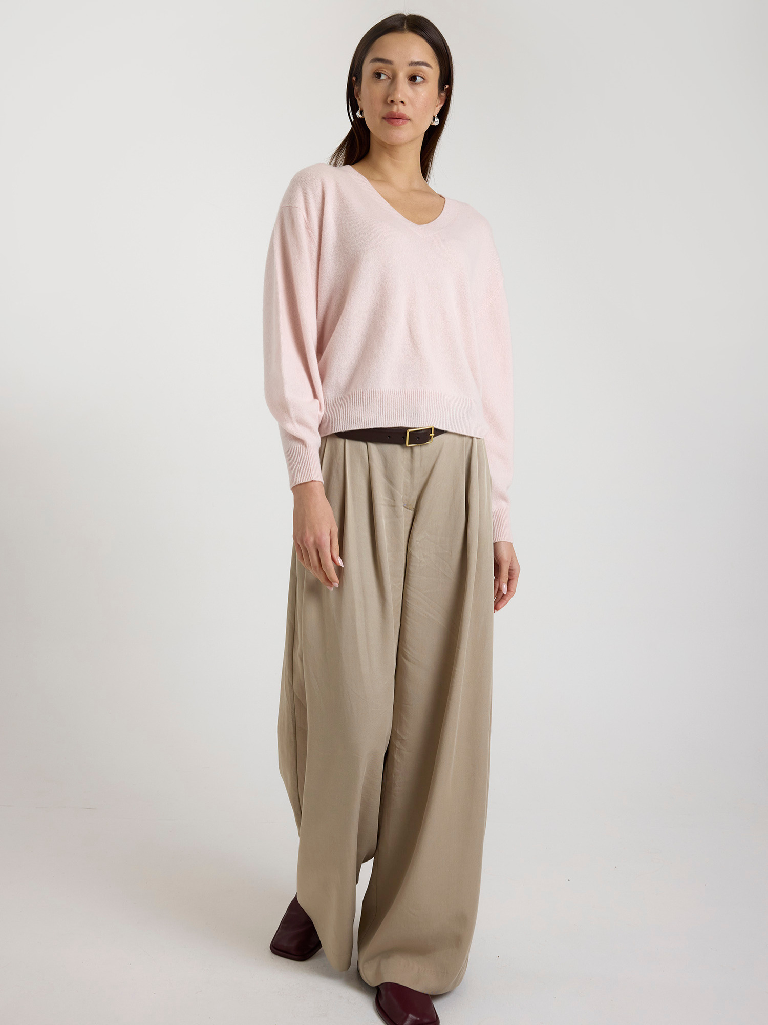 Woman wearing a light pink sweater and beige wide-leg pants on a white background