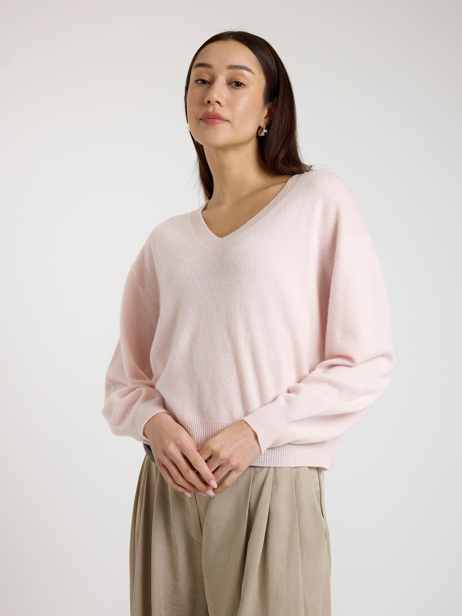 Woman wearing a light pink sweater and beige pants against a white background