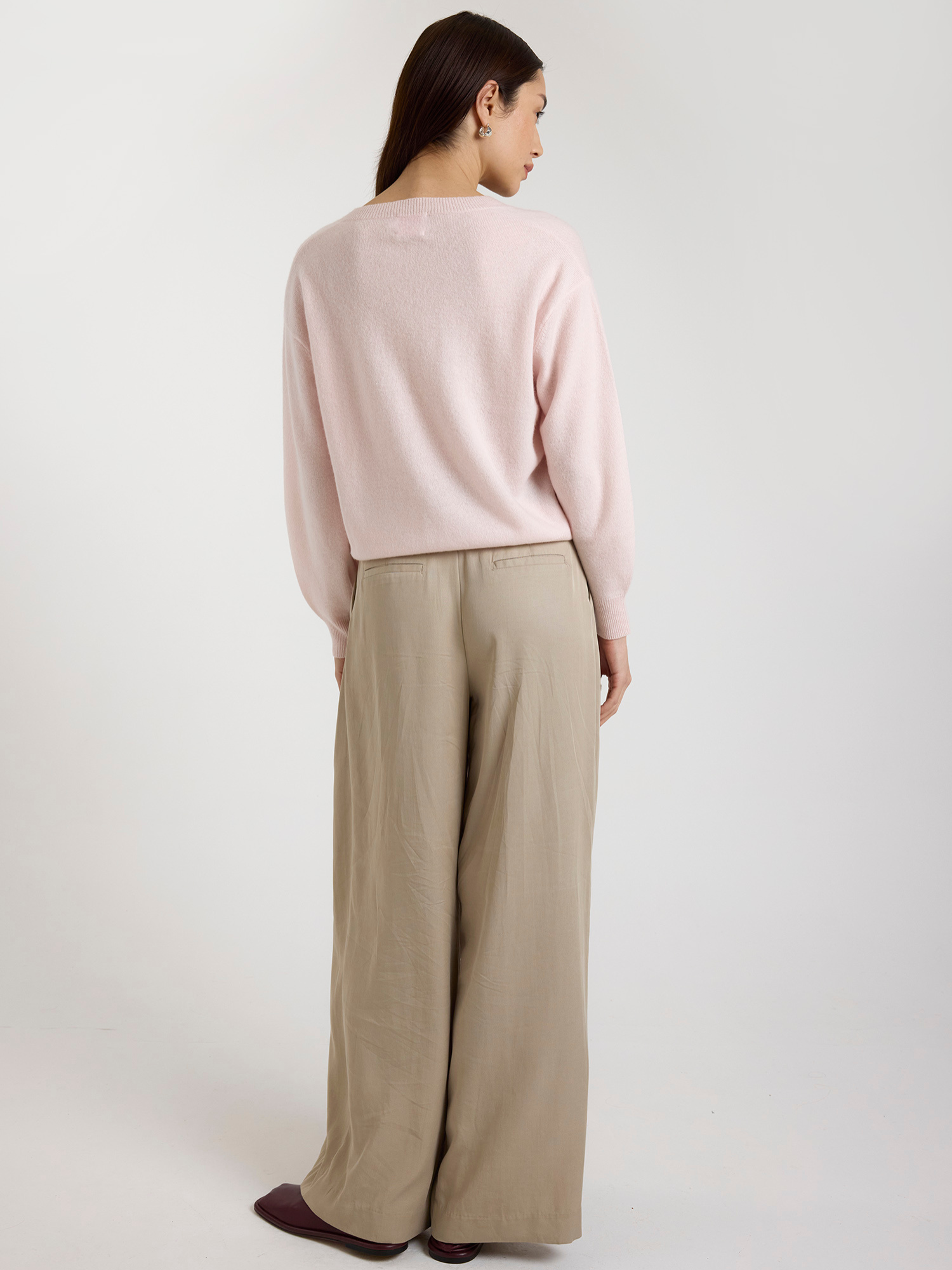 Woman wearing a light pink sweater and beige wide-leg pants on a white background