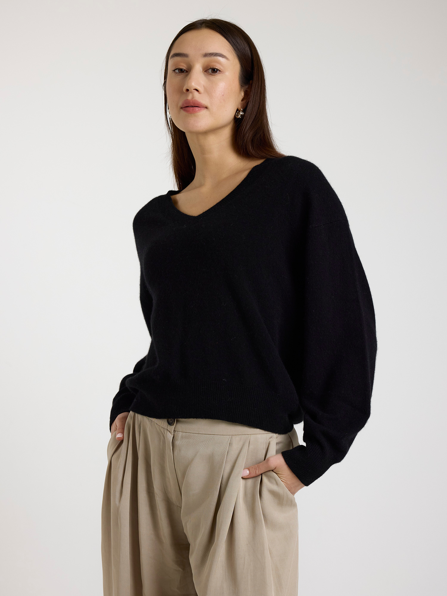 Woman wearing a black sweater and beige pants against a white background