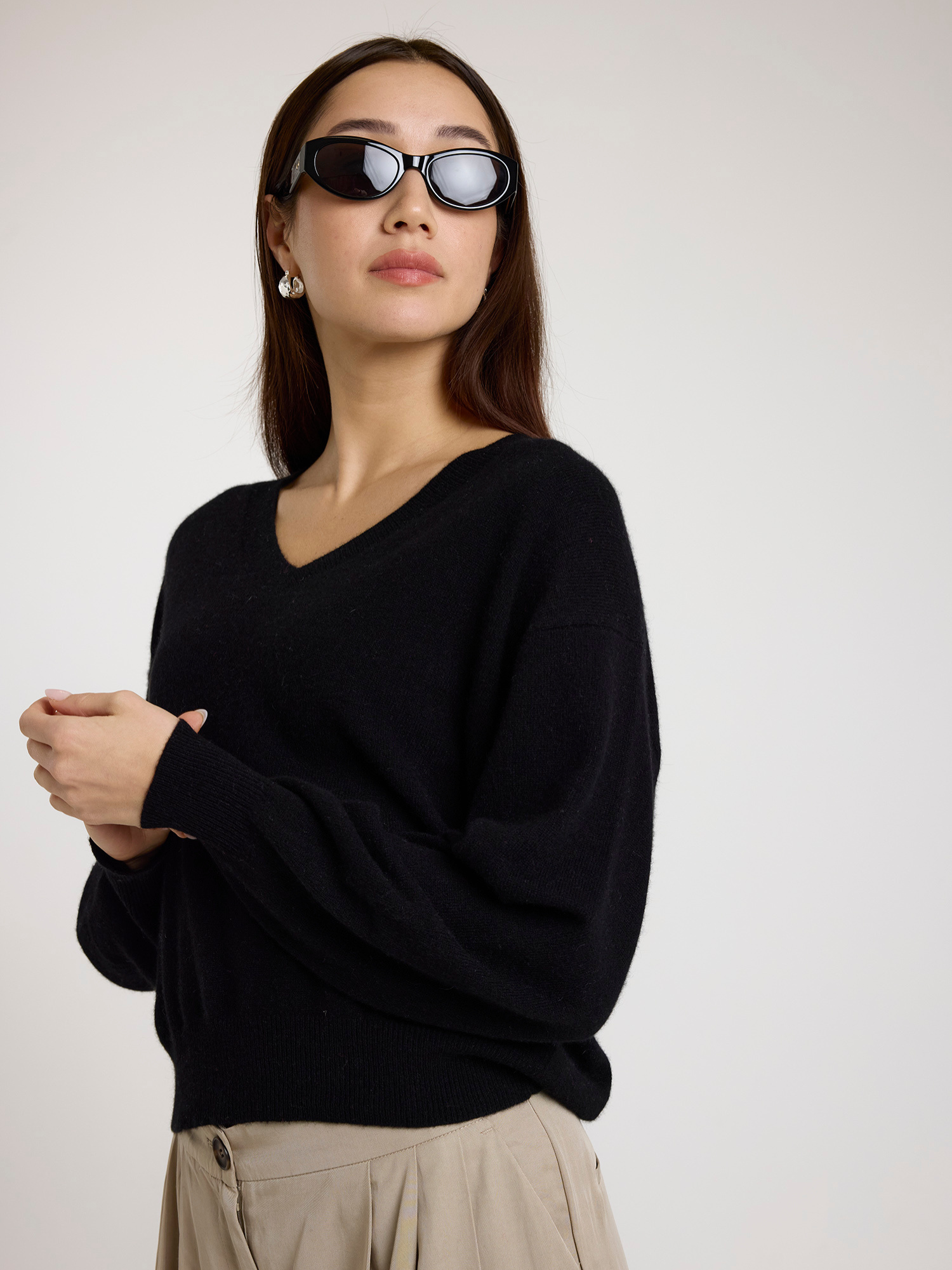 Woman wearing a black sweater and sunglasses against a plain background