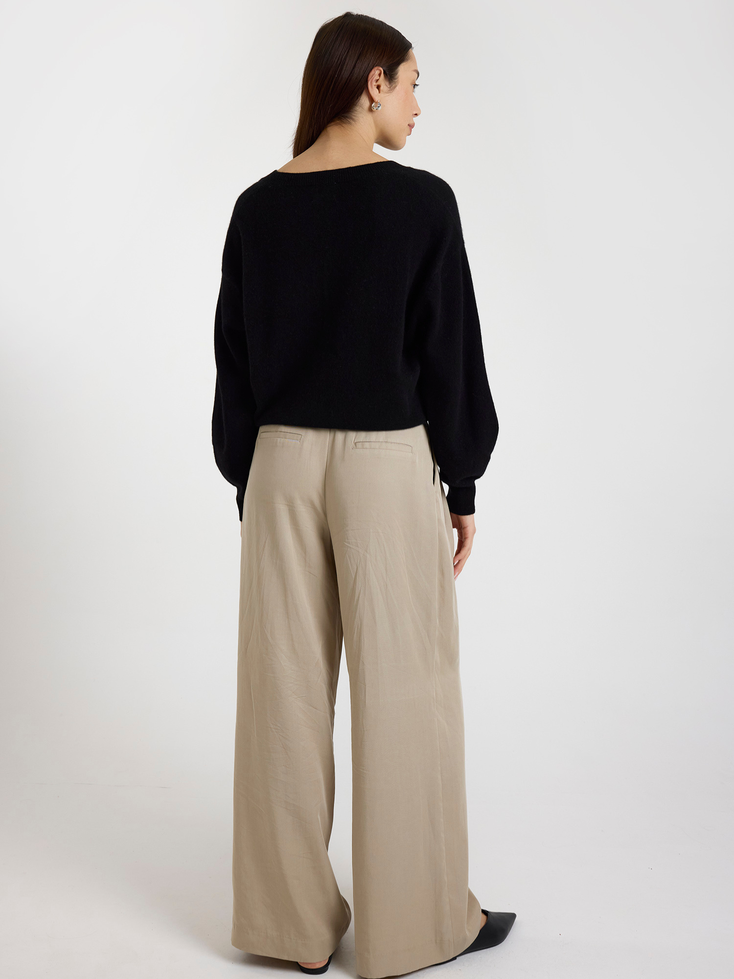 Woman wearing a black sweater and beige pants on a white background