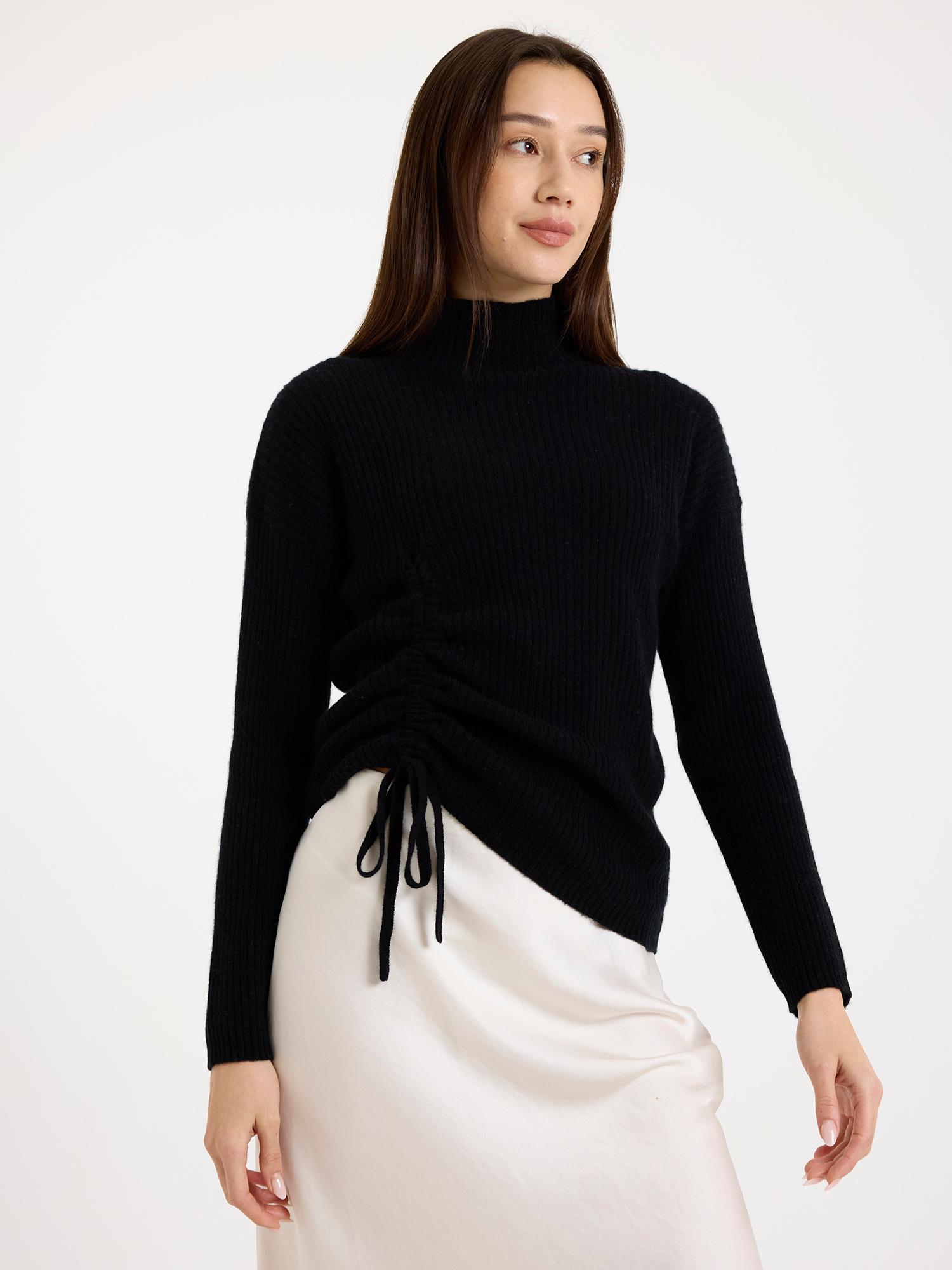 Woman wearing a black ribbed sweater and white skirt on a light background