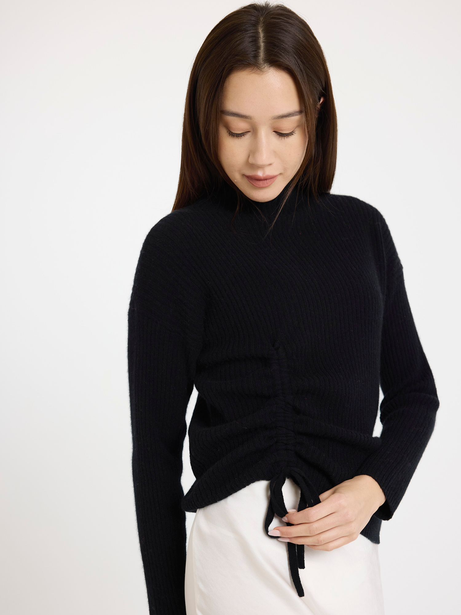 Woman wearing a black sweater with tie detail on a white background