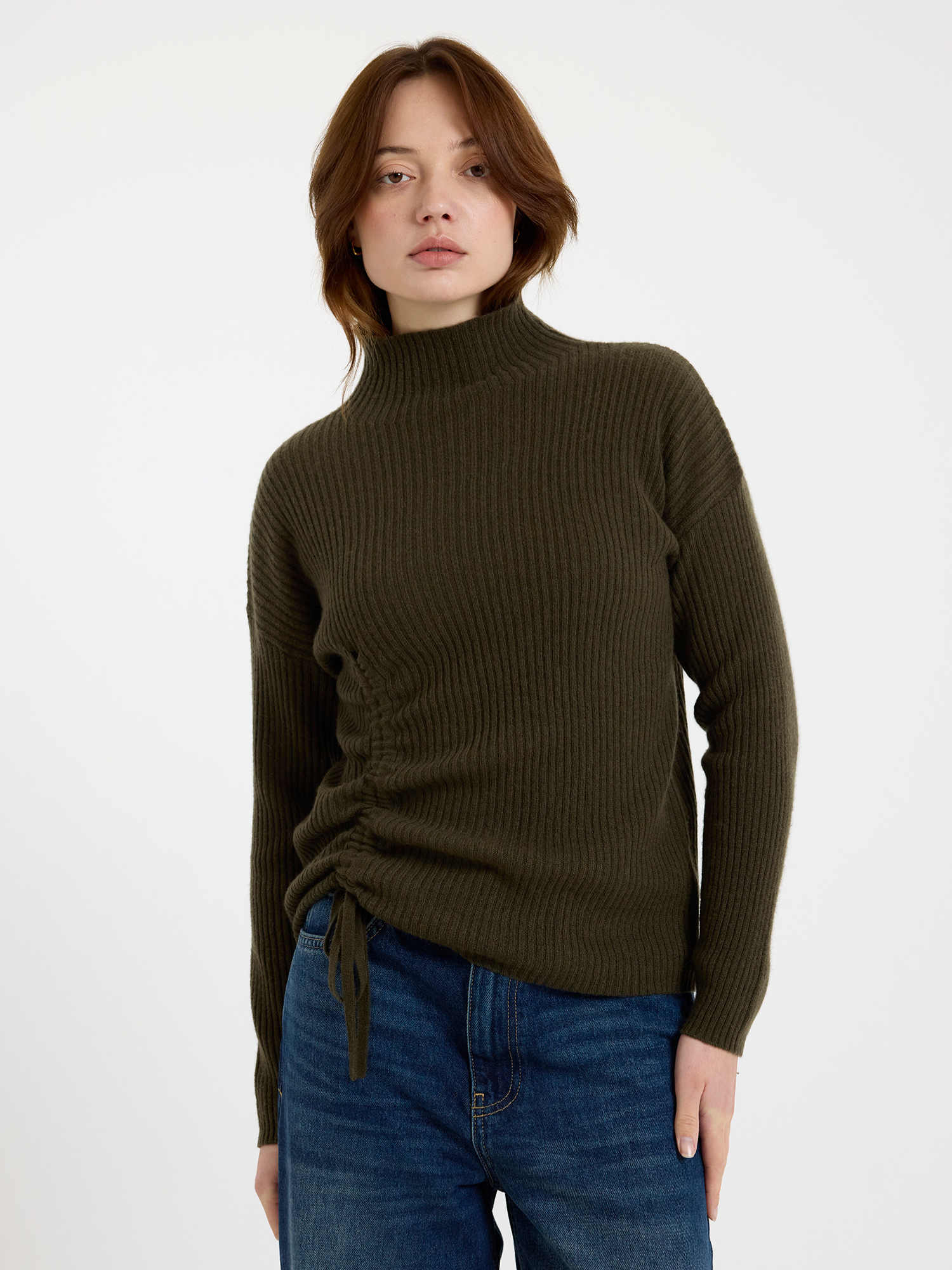 Woman wearing a green ribbed sweater and blue jeans on a white background