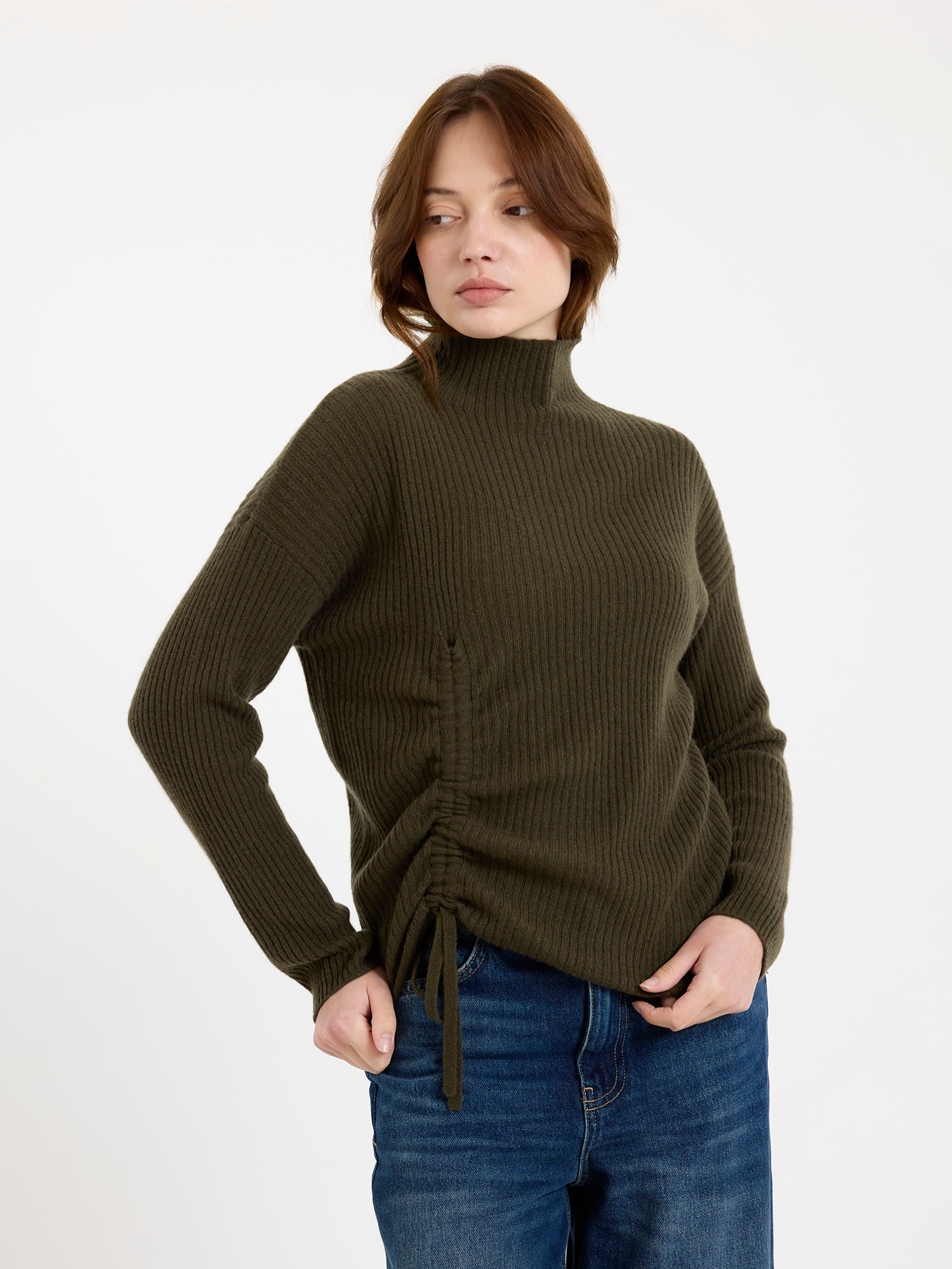 Woman wearing a green ribbed sweater with a tie detail on a white background