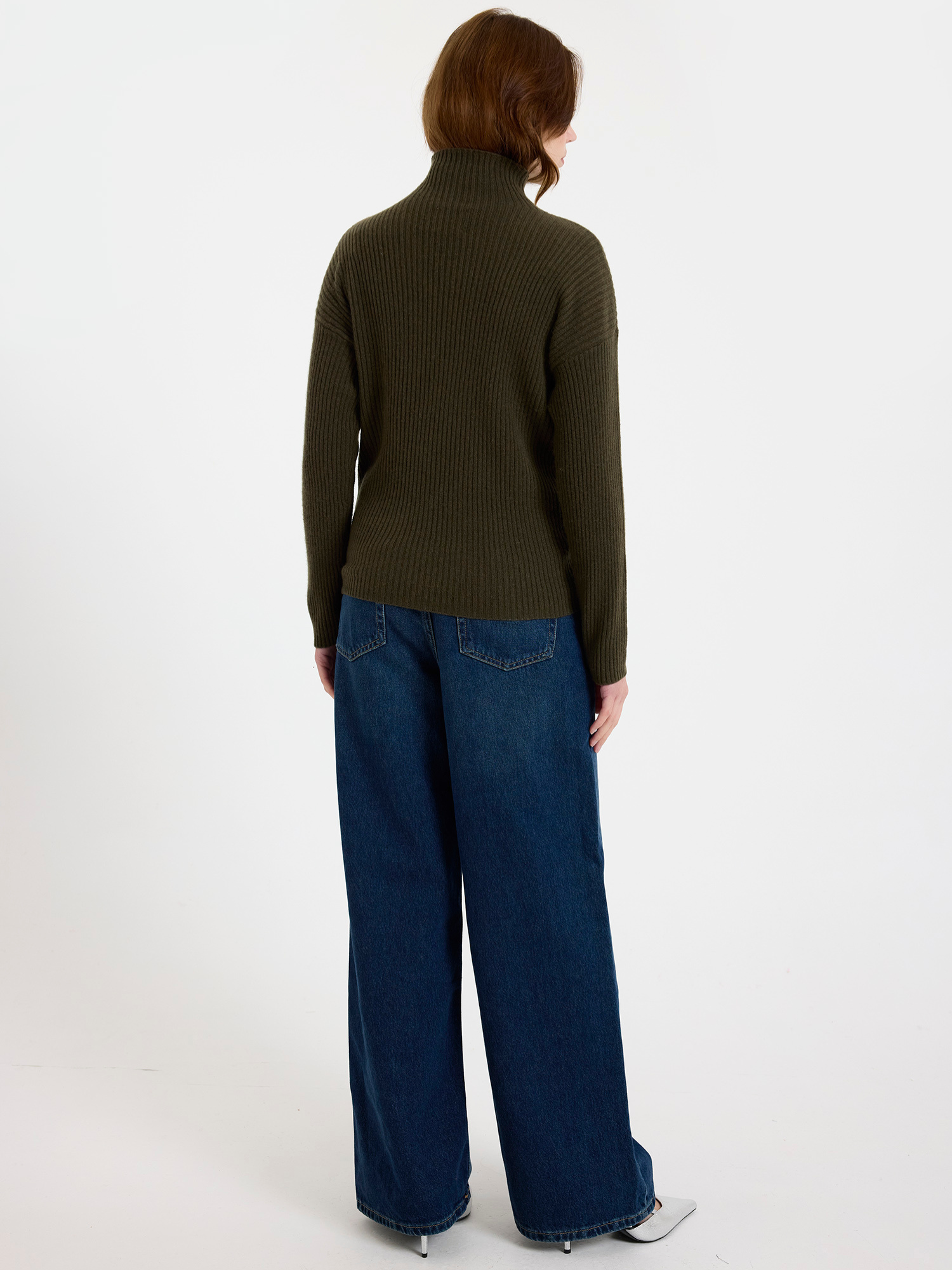 Woman wearing a green ribbed sweater and blue jeans on a white background
