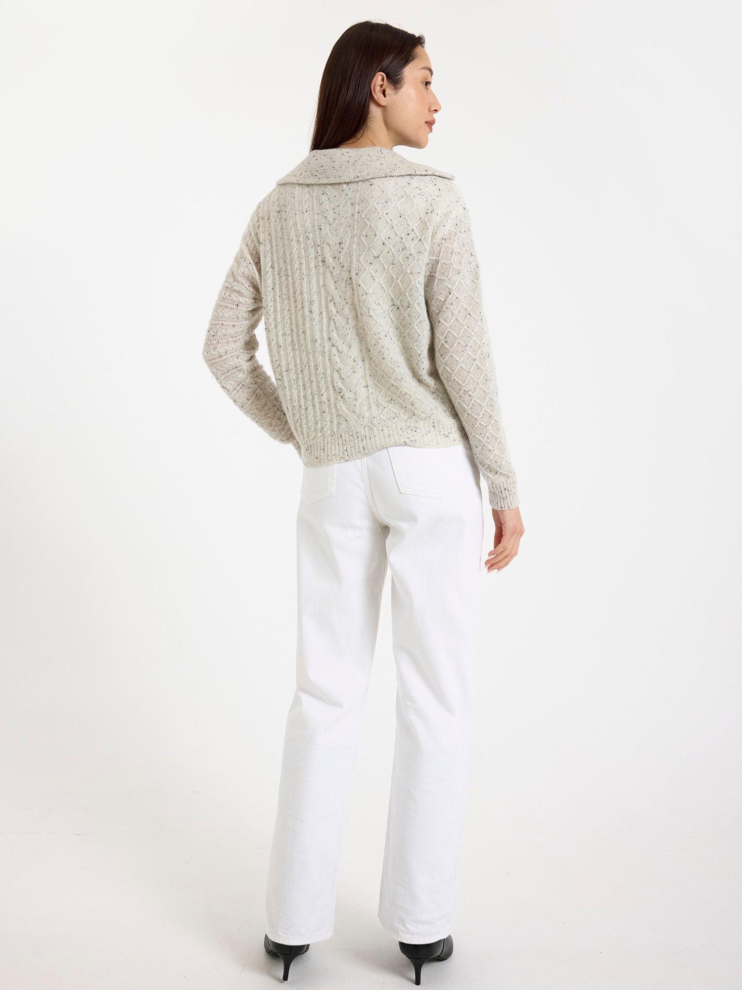 Woman wearing a grey speckled half zip-up sweater and white pants on a white background
