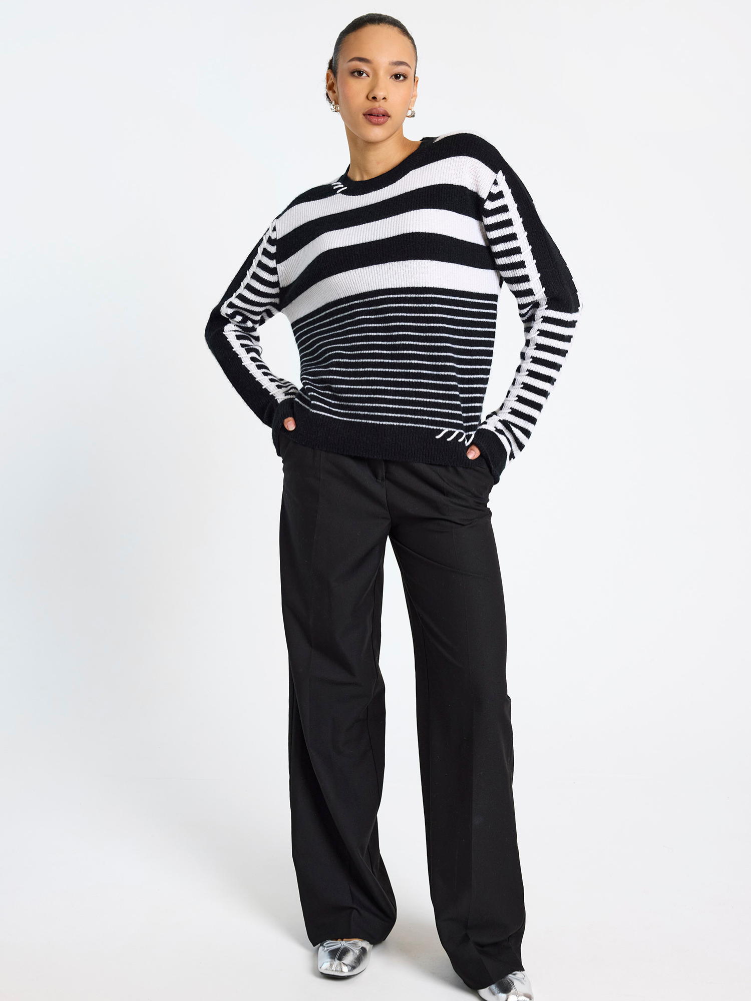 Woman wearing a black and white striped sweater with black pants on a white background