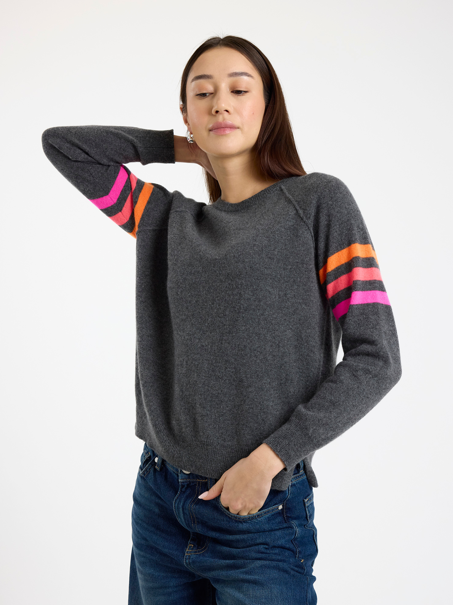 Woman wearing a dark grey sweater with colourful stripe sleeves on a white background