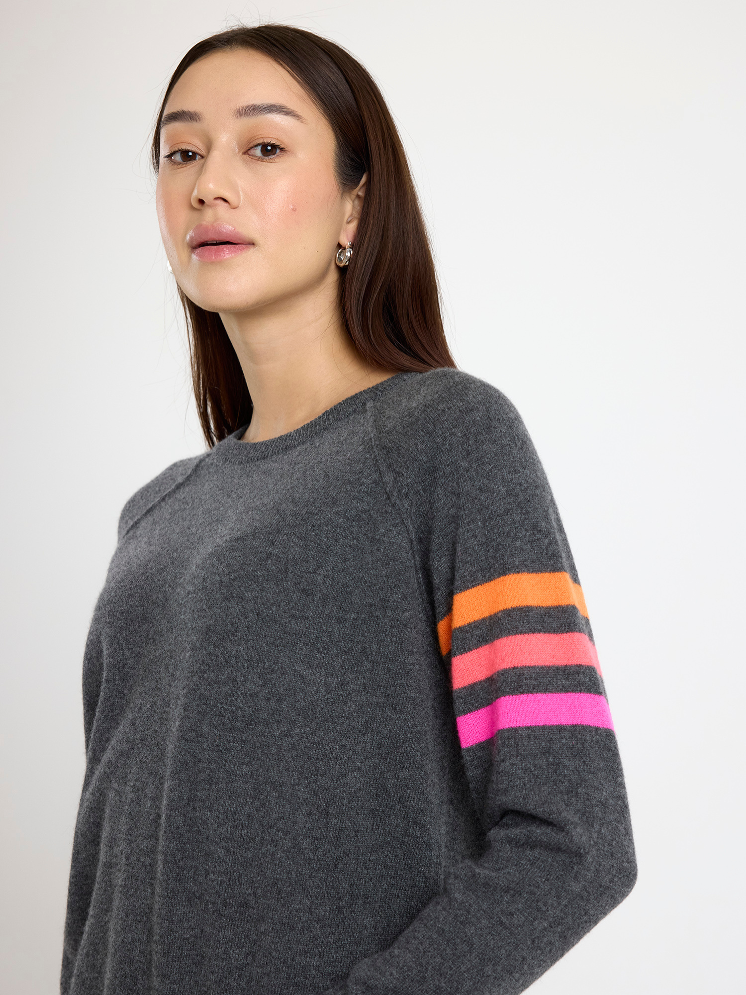 Woman wearing a dark grey sweater with colourful stripes on a white background
