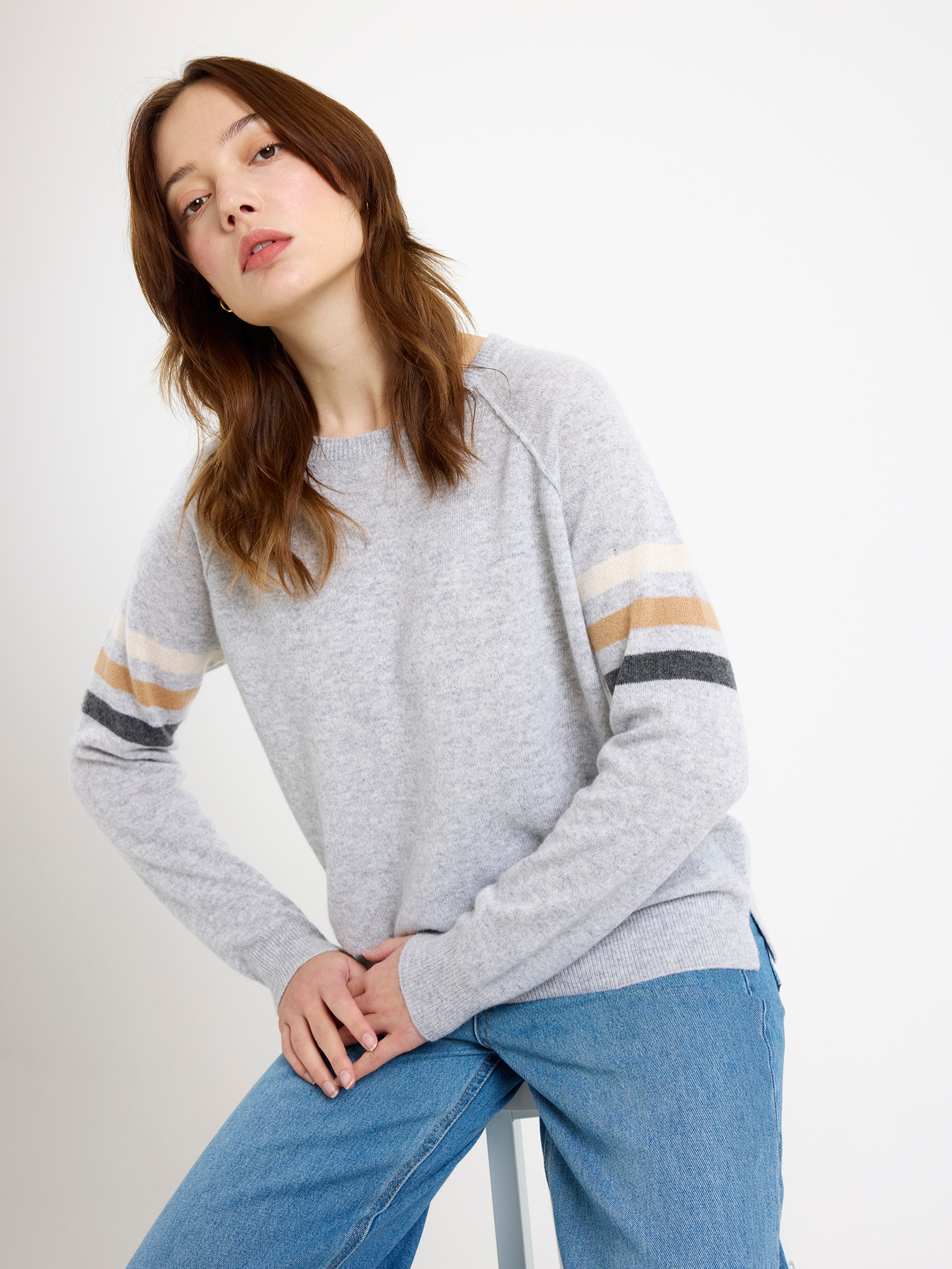 Woman wearing a gray sweater with striped sleeves and blue jeans on a white background