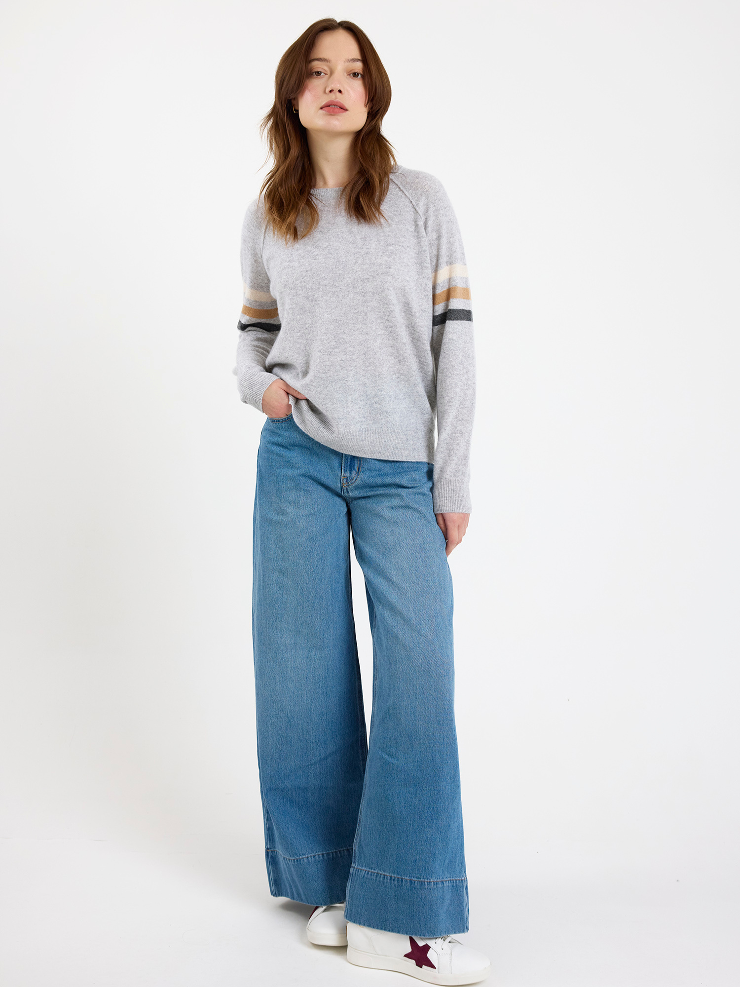 Woman wearing a gray sweater with striped sleeves and blue jeans on a white background