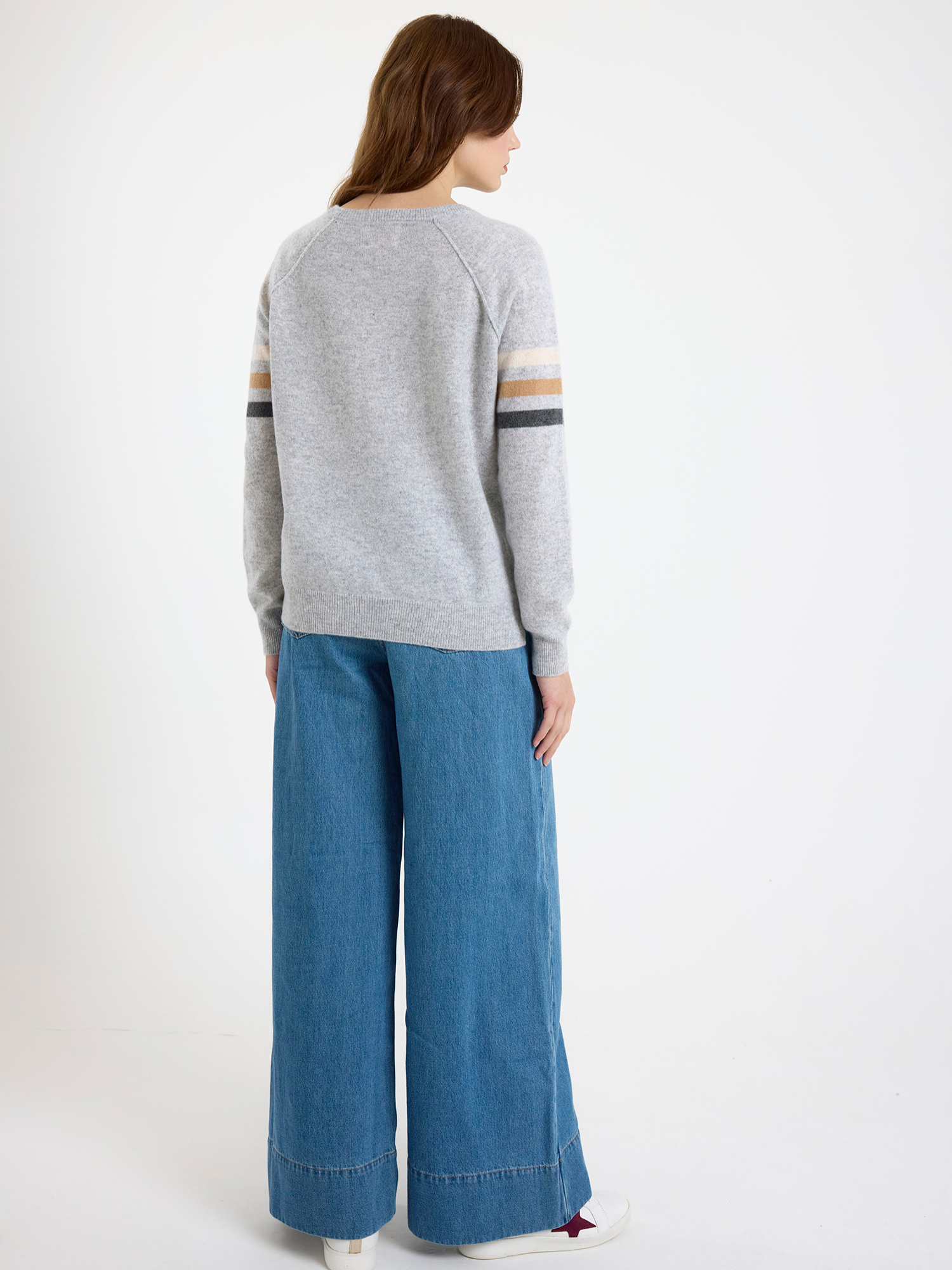Women wearing a grey sweater with striped sleeves and blue wide-leg jeans on a white background