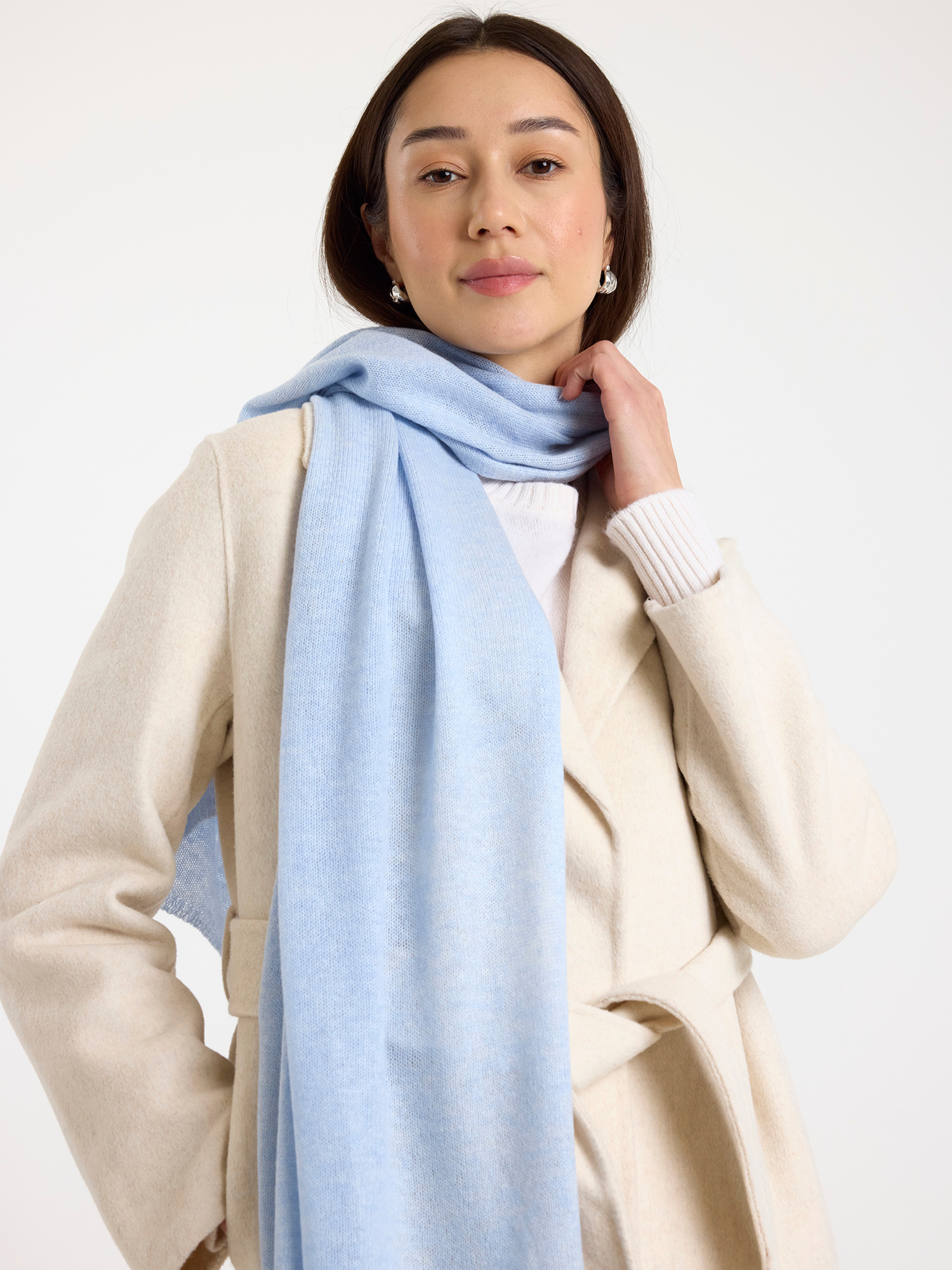 Woman wearing a light blue scarf and beige coat on a white background