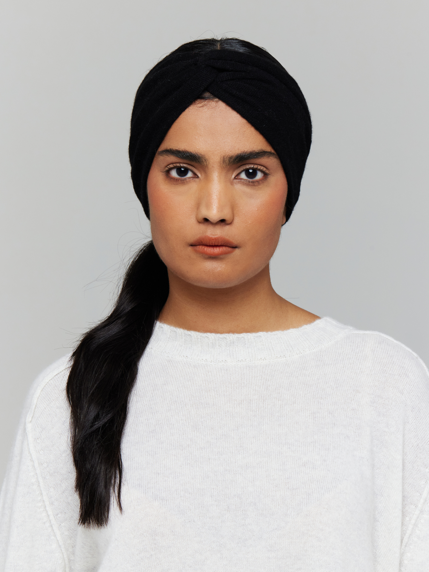 Woman wearing a black knitted headband and white sweater against a grey background