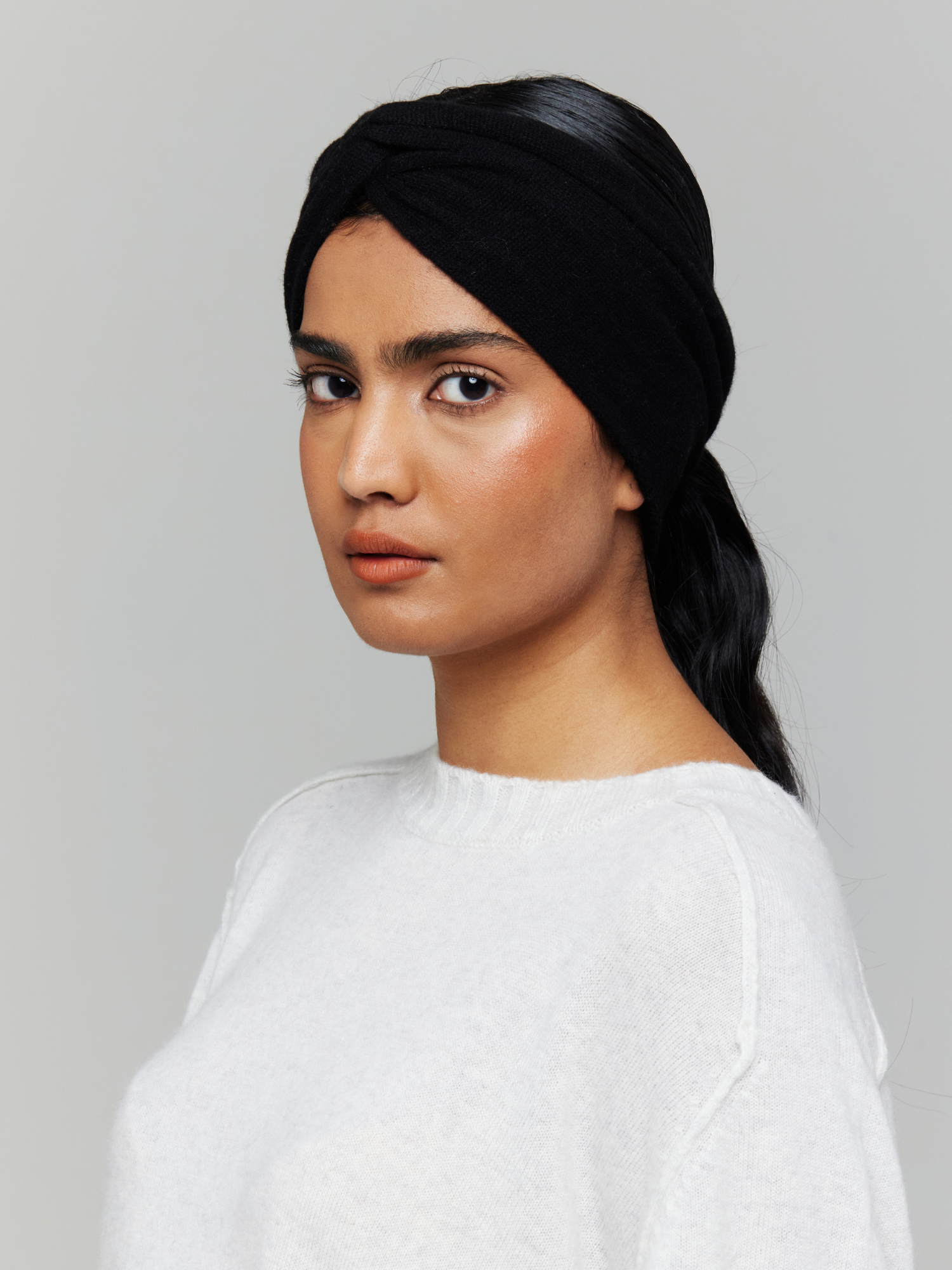 Woman wearing a black knitted headband and white top against a grey background