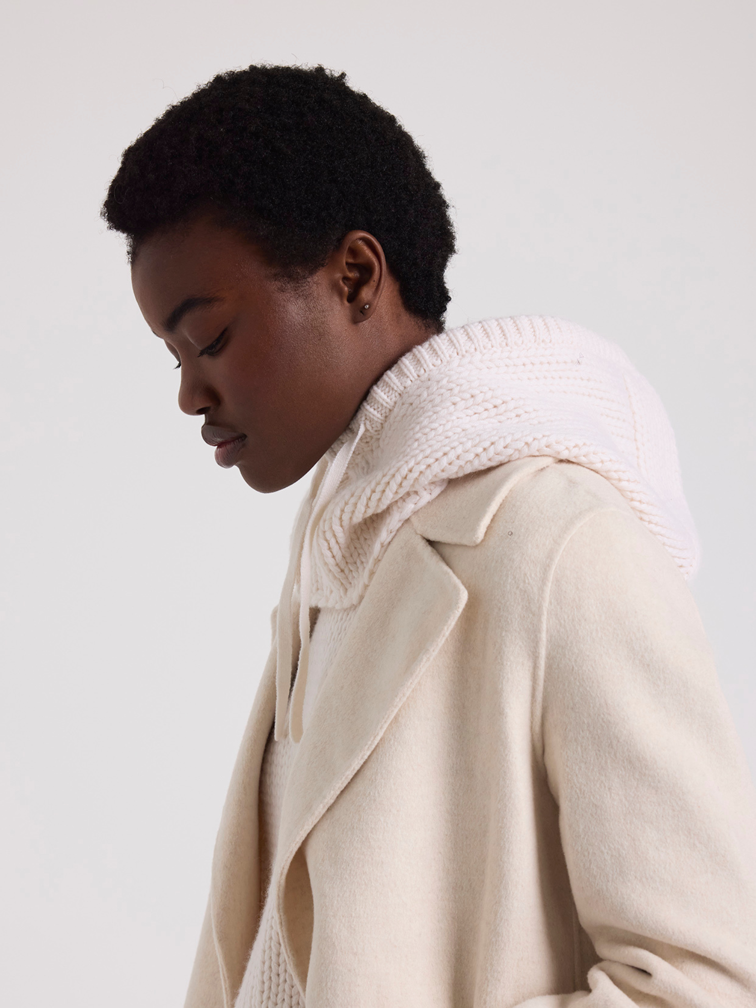 Person wearing a white knitted balaclava over a beige coat on a plain background