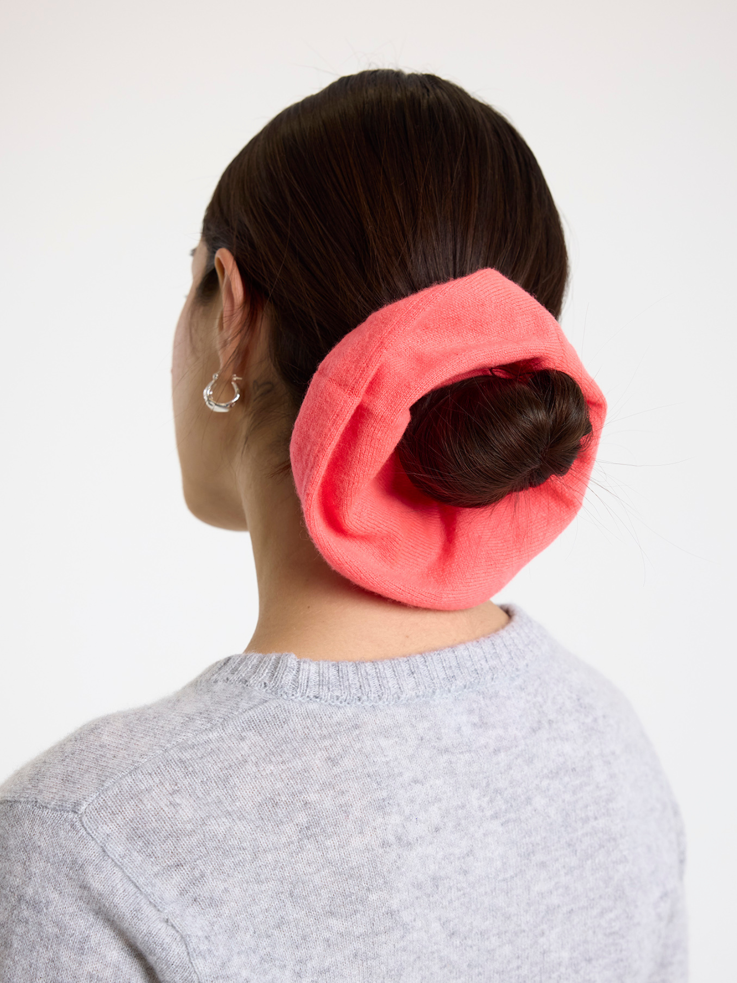 Person wearing a pink scrunchie in their hair on a white background