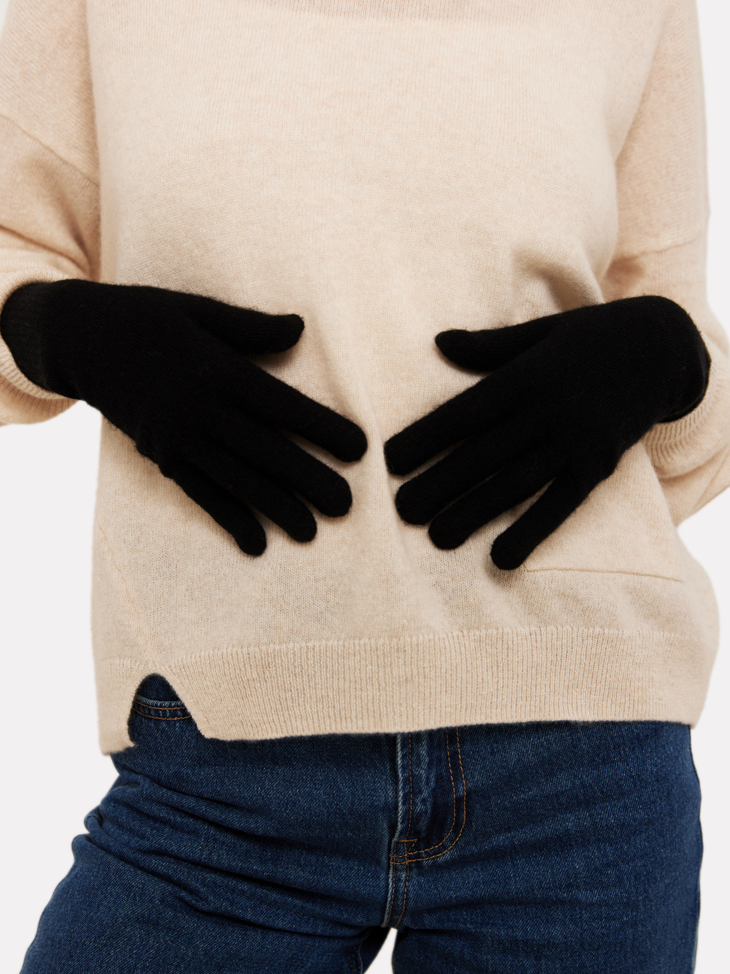 Person wearing black gloves with a beige sweater and blue jeans on a white background