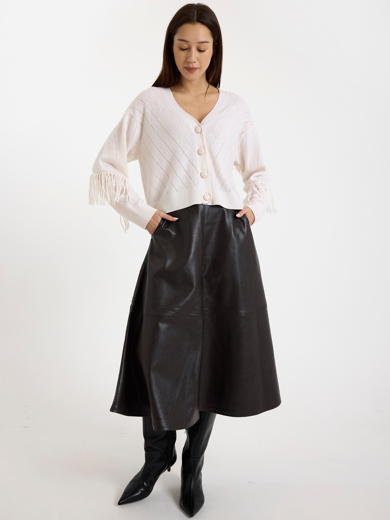 Woman wearing a white fringed cardigan with a brown leather skirt on a white background