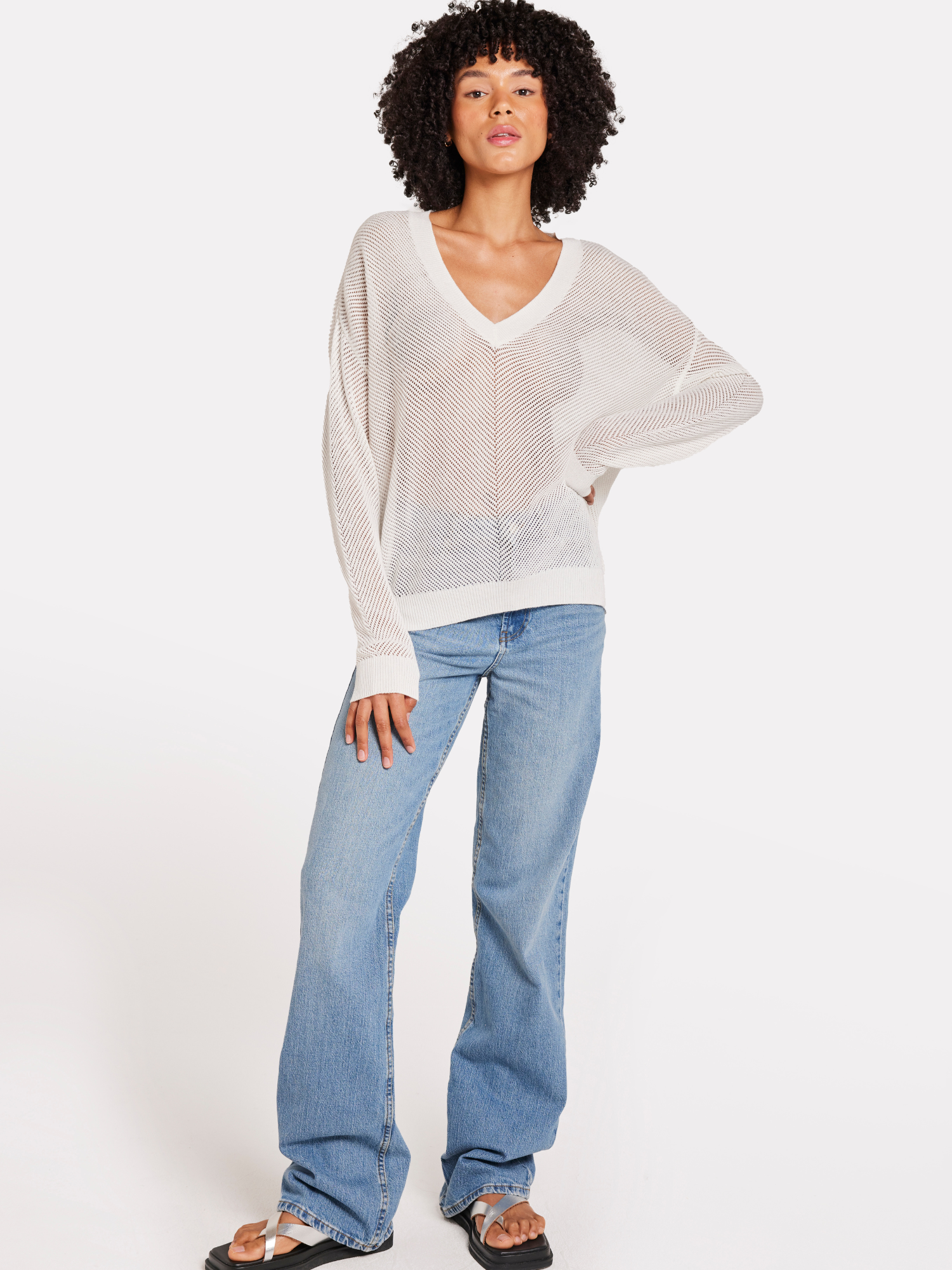 A woman wearing a white V-neck jumper with pointelle chevron detail with blue jeans