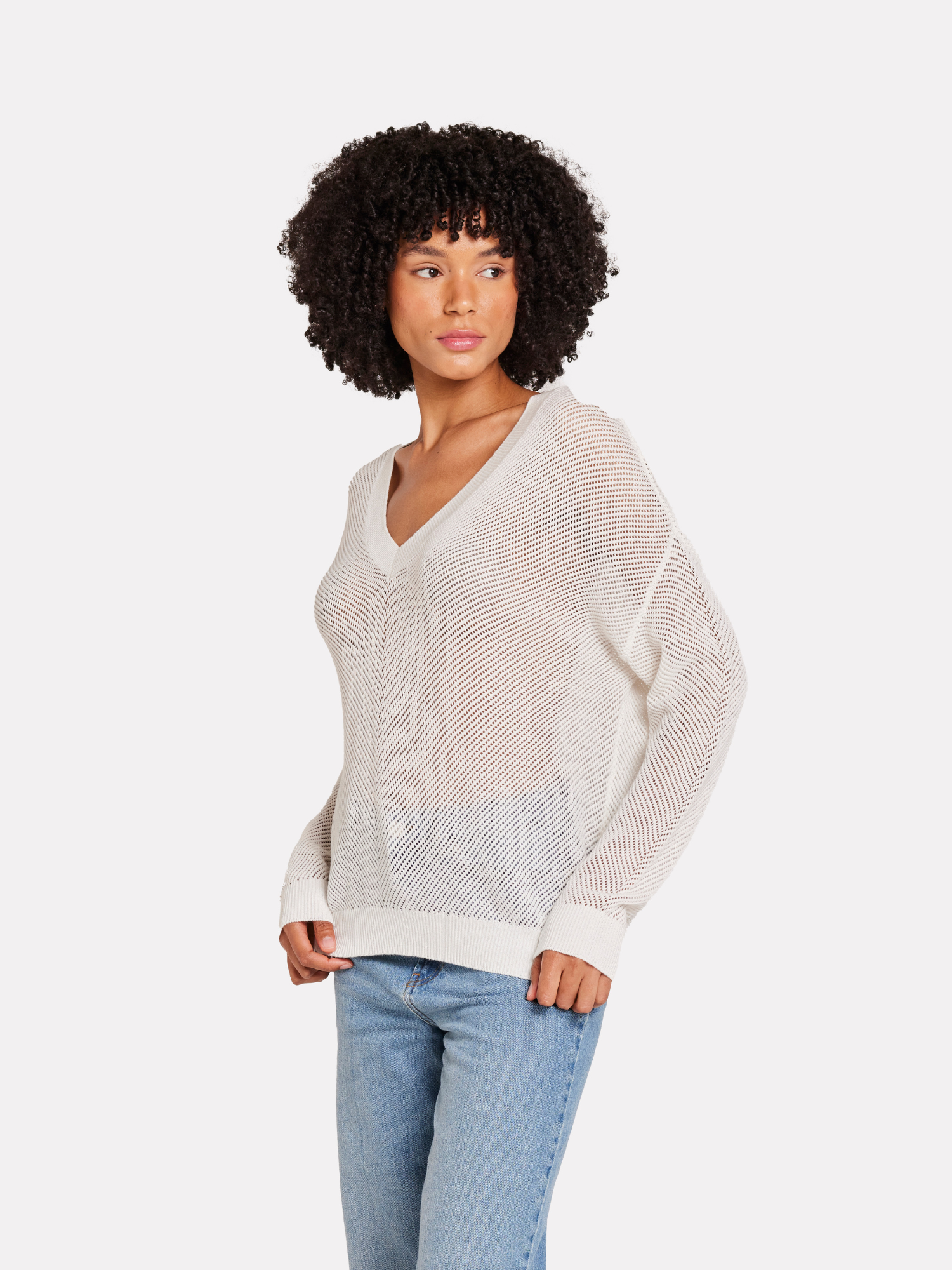 A woman wearing a white V-neck jumper with pointelle chevron detail with blue jeans