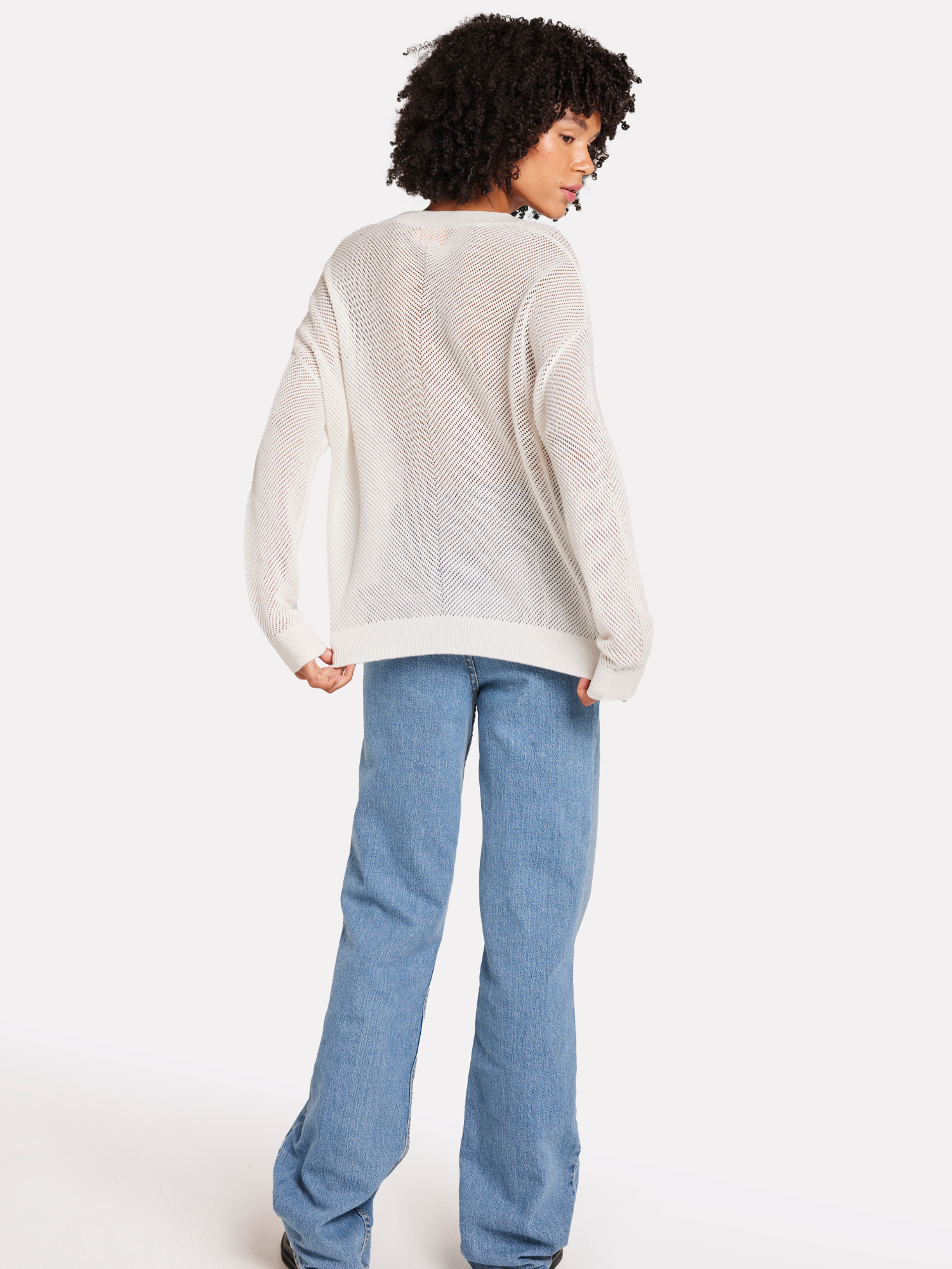 A woman wearing a white V-neck jumper with pointelle chevron detail with blue jeans