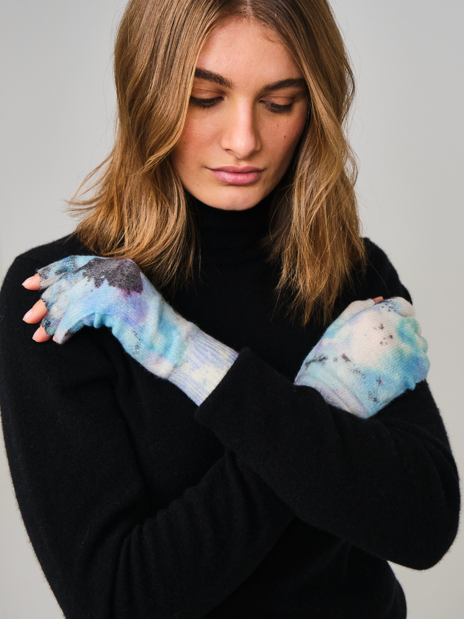 Woman wearing black sweater and colorful gloves against a gray background