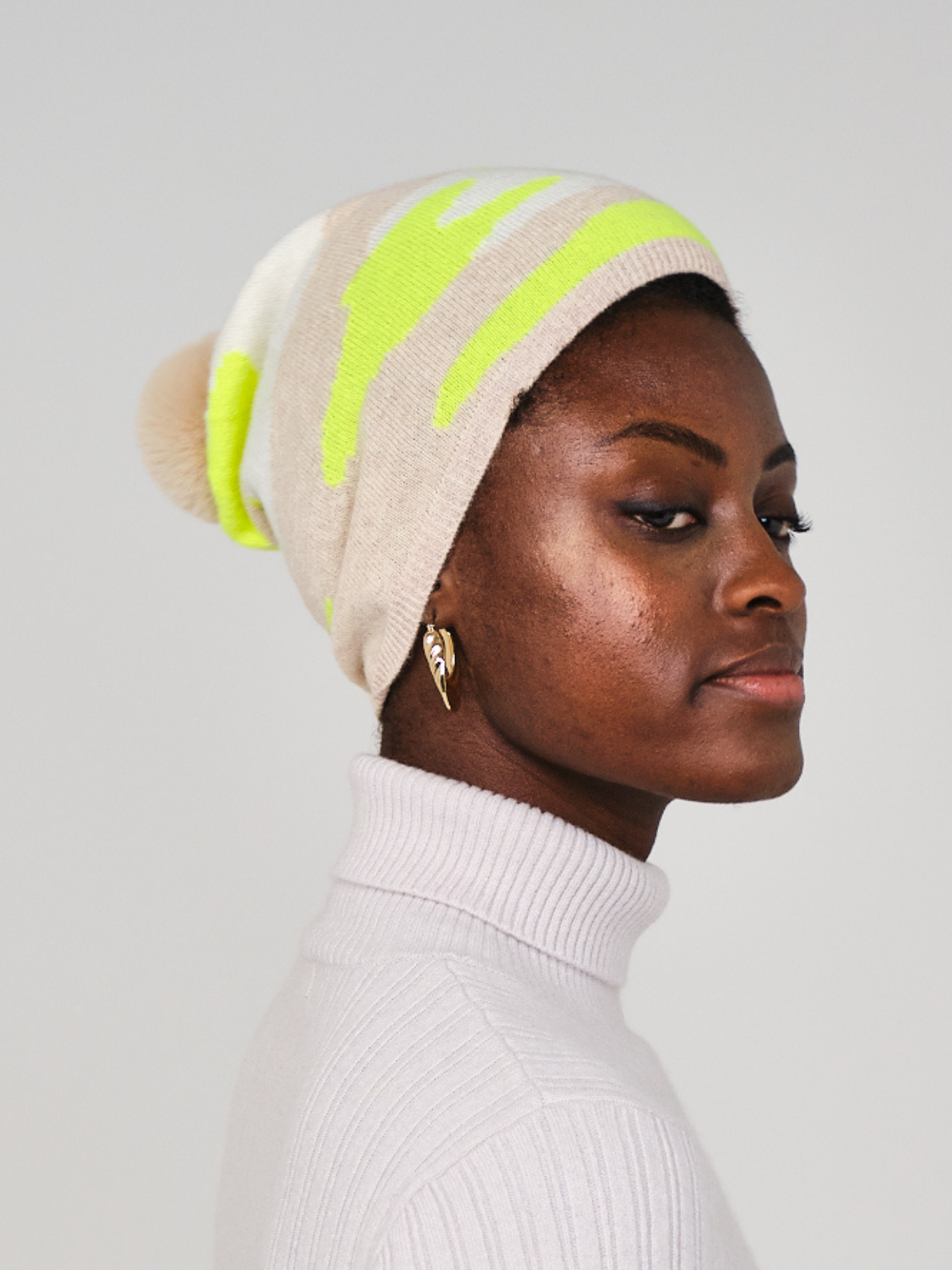 women wearing a beige and yellow camo pattern hat with a pom pom