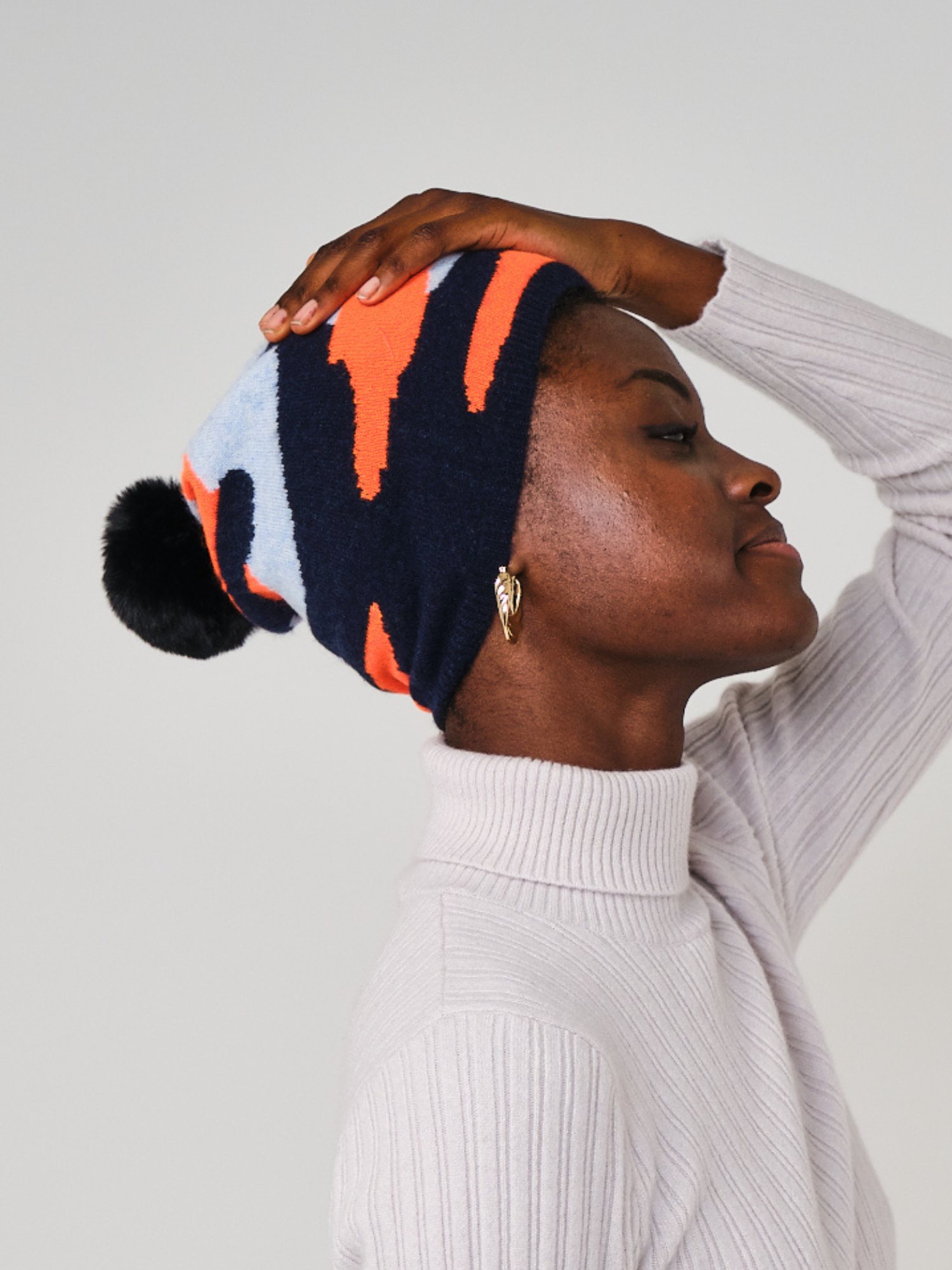 women wearing a navy, orange and light blue camo pattern hat with a pom pom